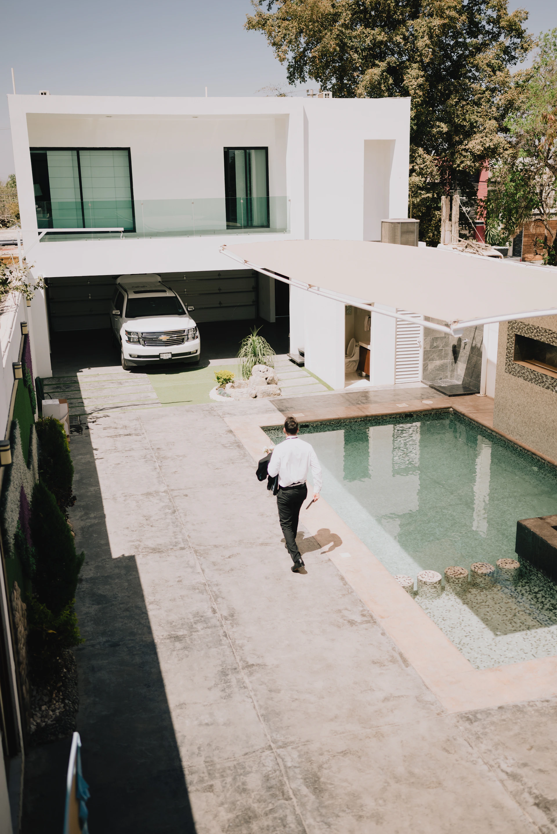 Man walks towards a swimming pool and modern house.