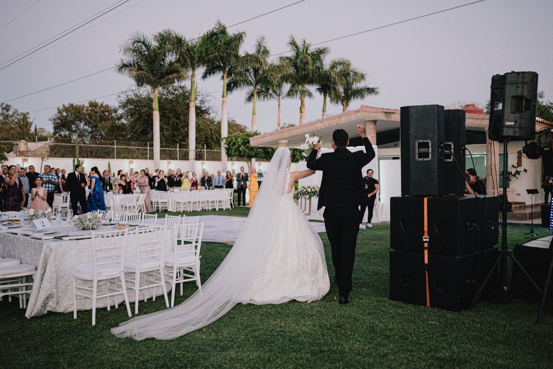 Newlyweds walk towards wedding reception with guests watching