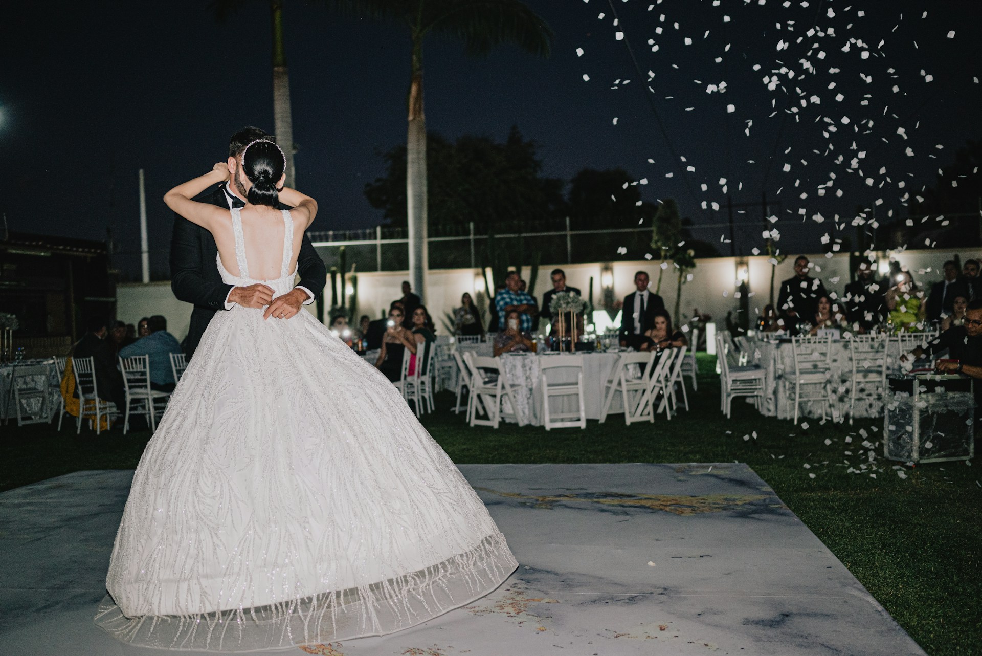 Bride and groom dancing under falling petals at night.
