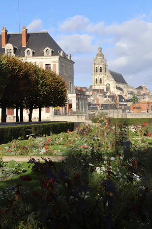 Ornate church tower overlooks blooming garden and buildings.