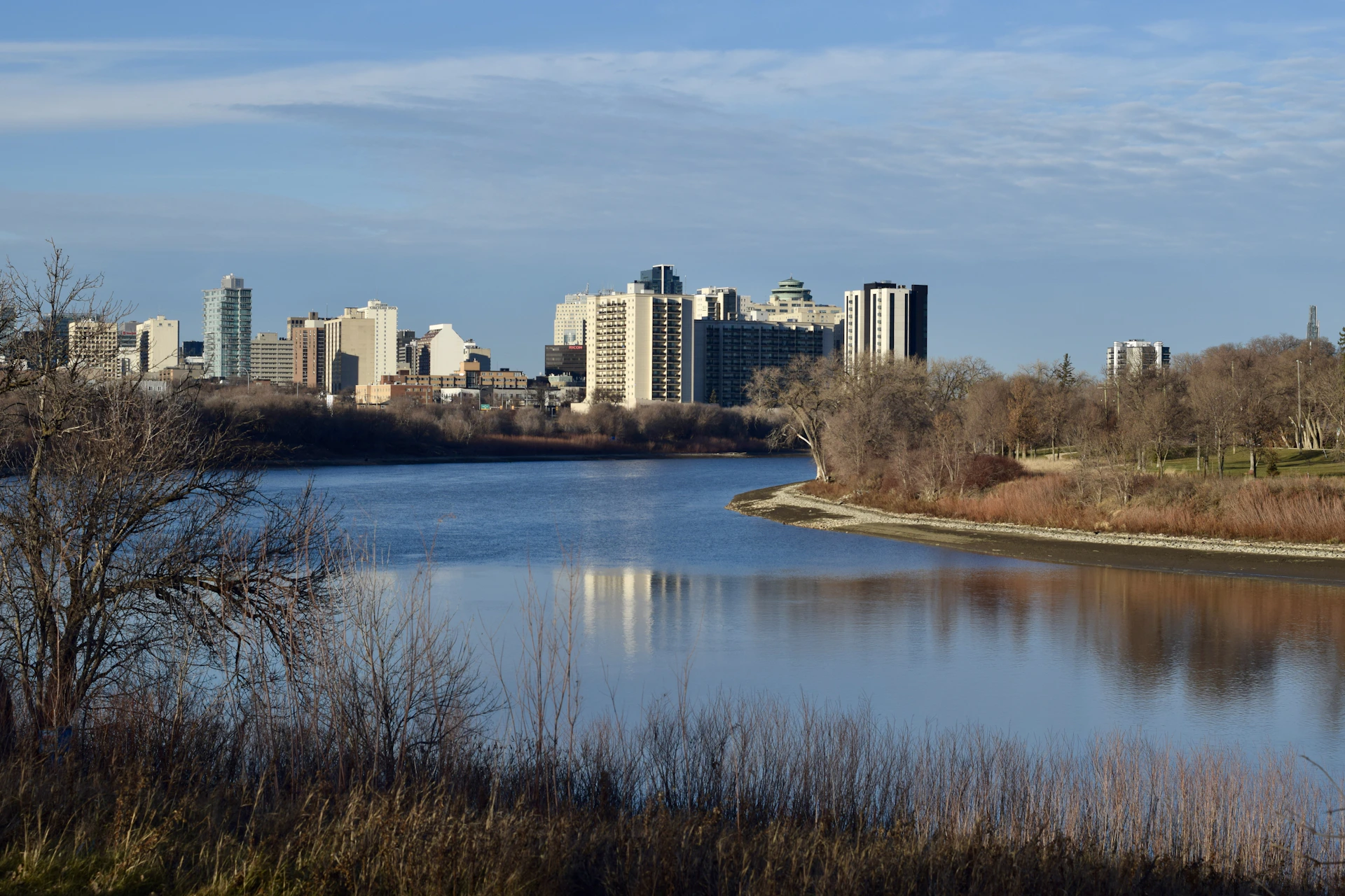 City skyline reflected in a calm river under blue sky.