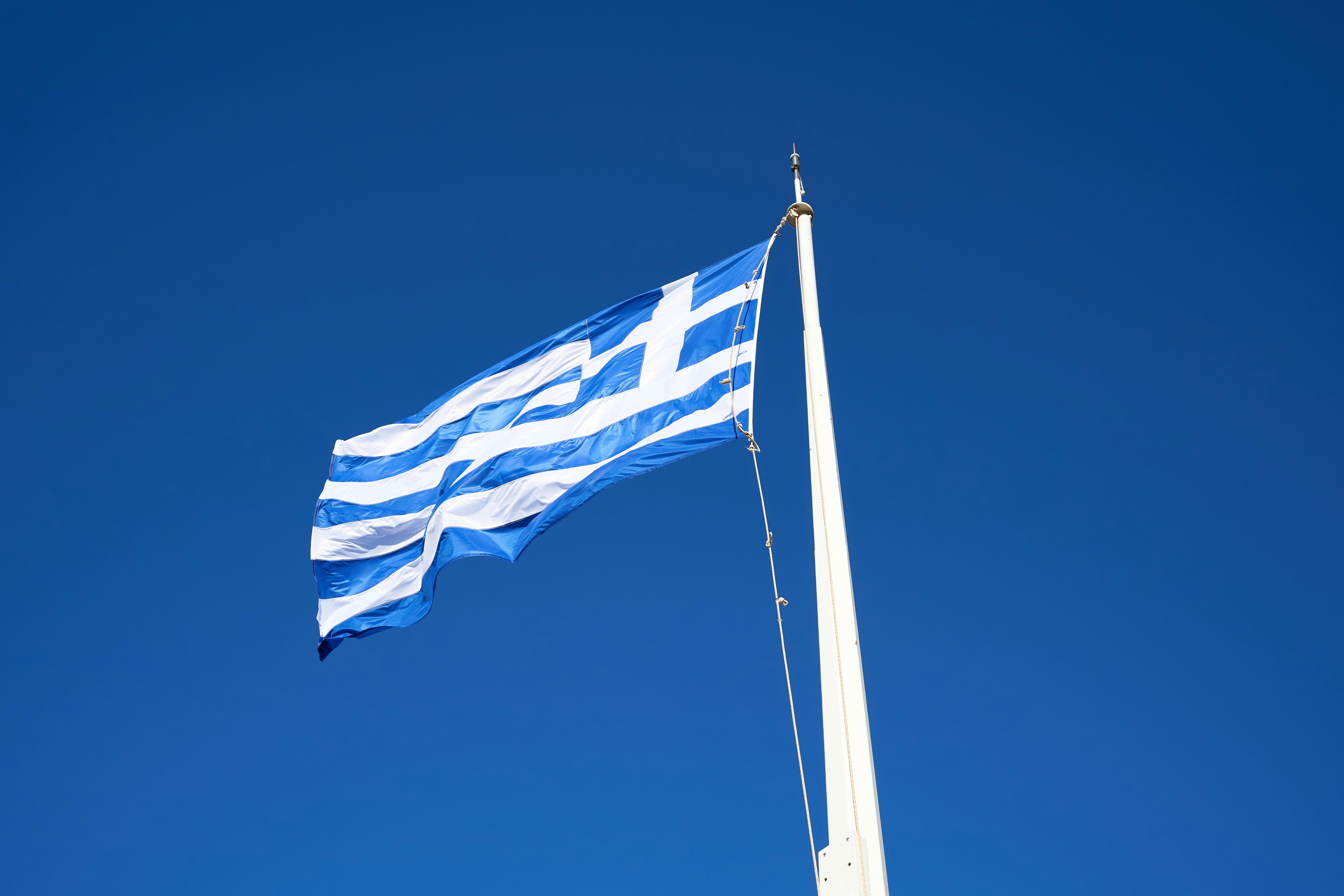 The greek flag waves proudly against a clear blue sky.