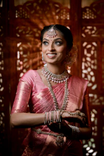 A smiling woman in a pink sari and jewelry.