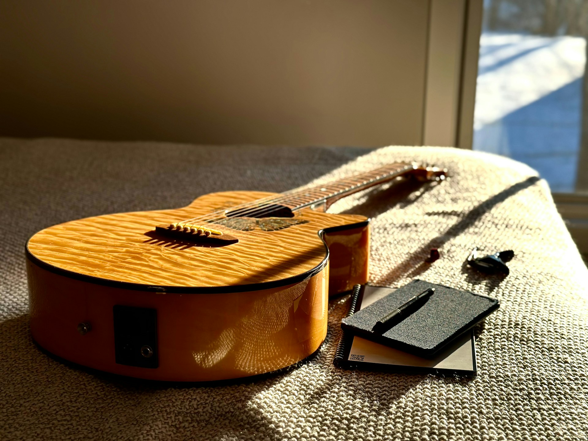 Acoustic guitar rests on a textured surface near window.