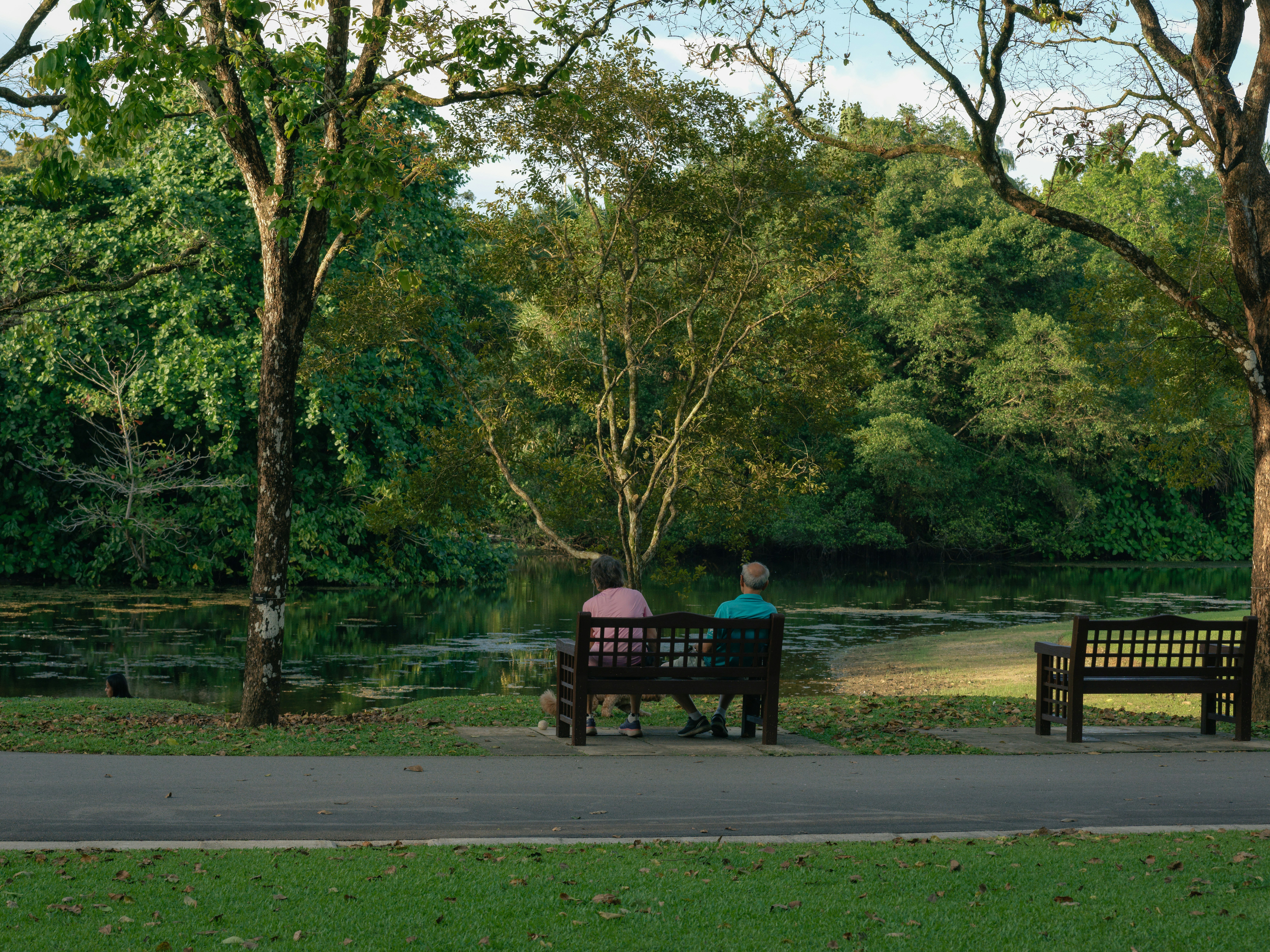 Two people sit on a park bench by a lake.