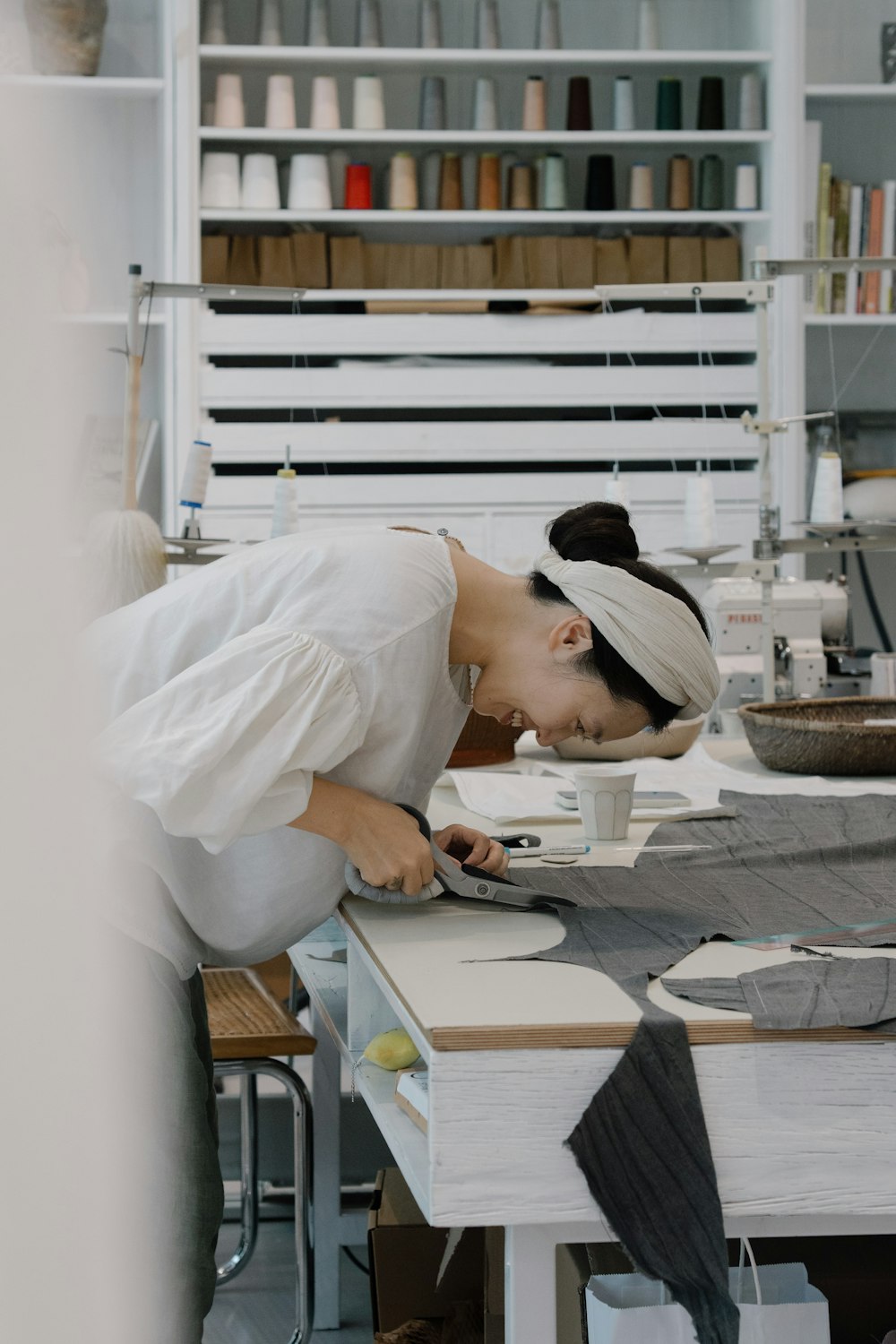 Cutter working over dark cloth on a long table inside a bright atelier