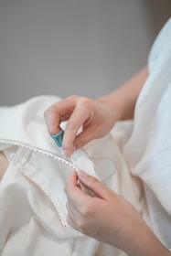 A person sewing white fabric with red trim.