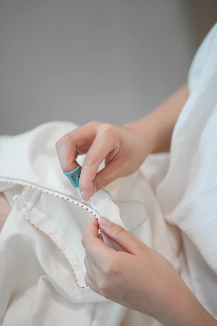 An artisan hand-sewing fine detail with needle and thread on white fabric