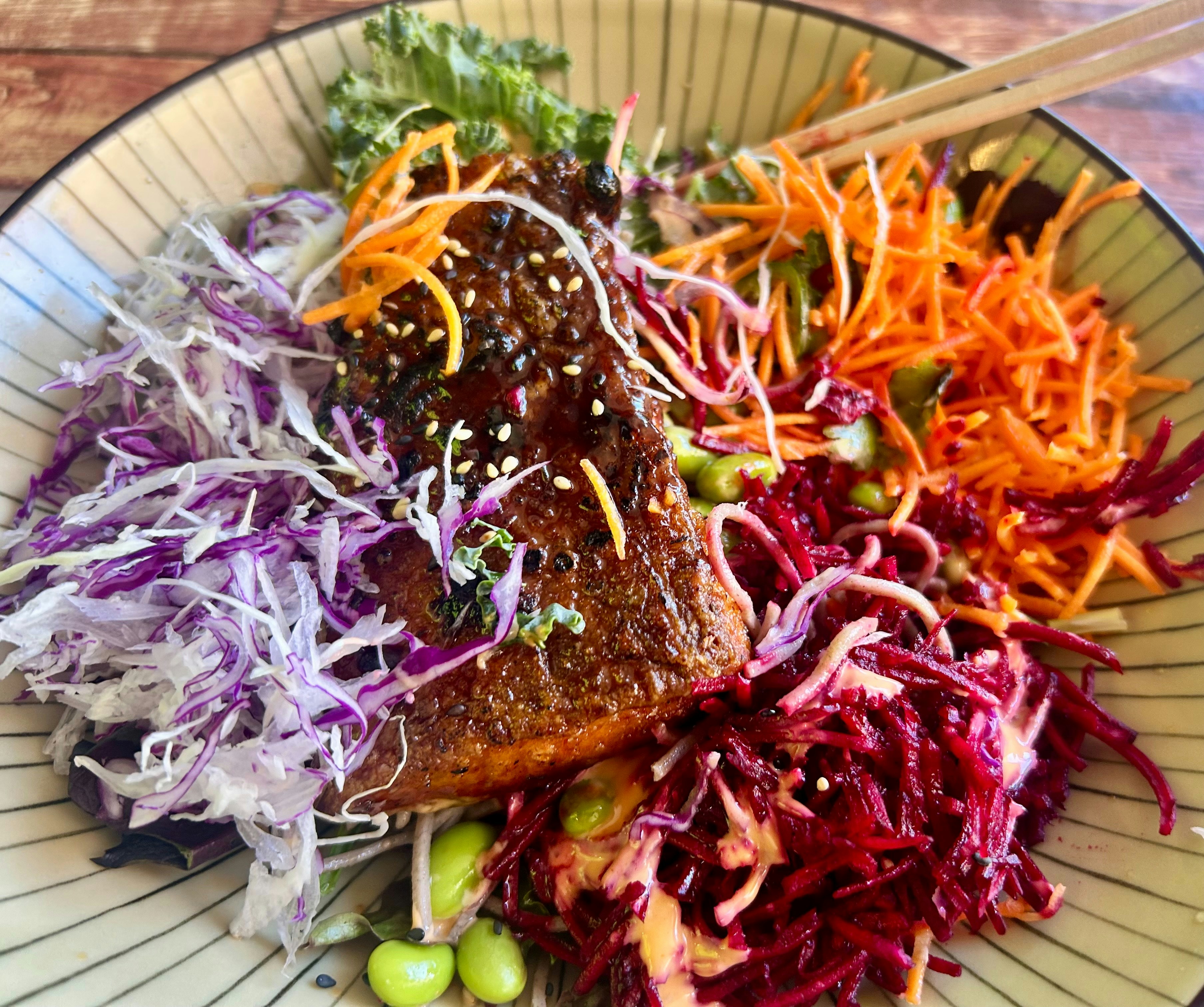 Salmon poke bowl with colorful vegetables and chopsticks