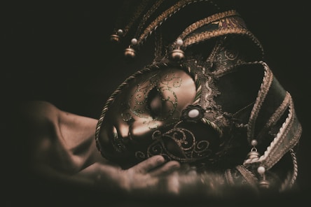 A hand holds an ornate venetian jester mask.