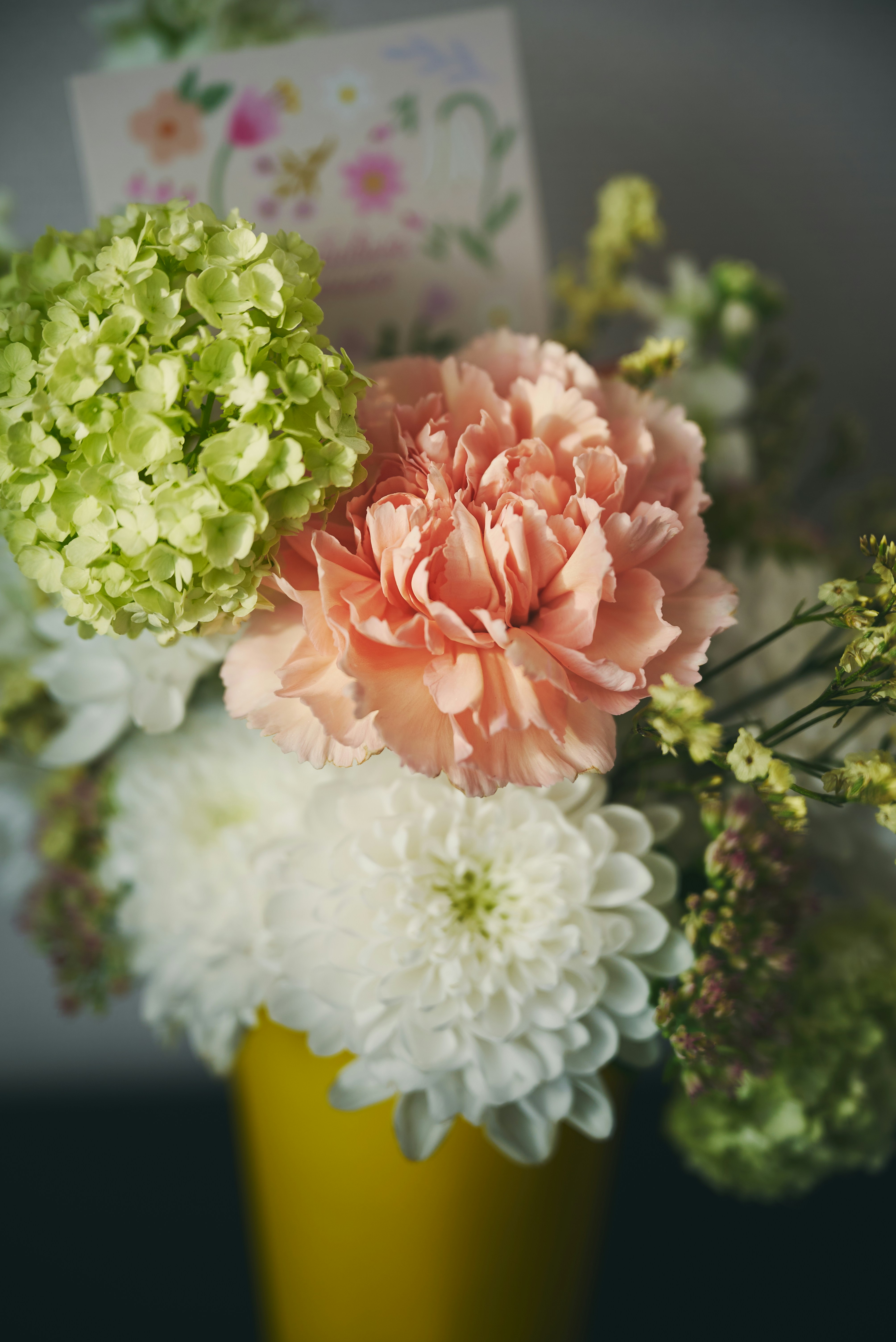 Bouquet of peach, white, and green flowers in yellow vase.