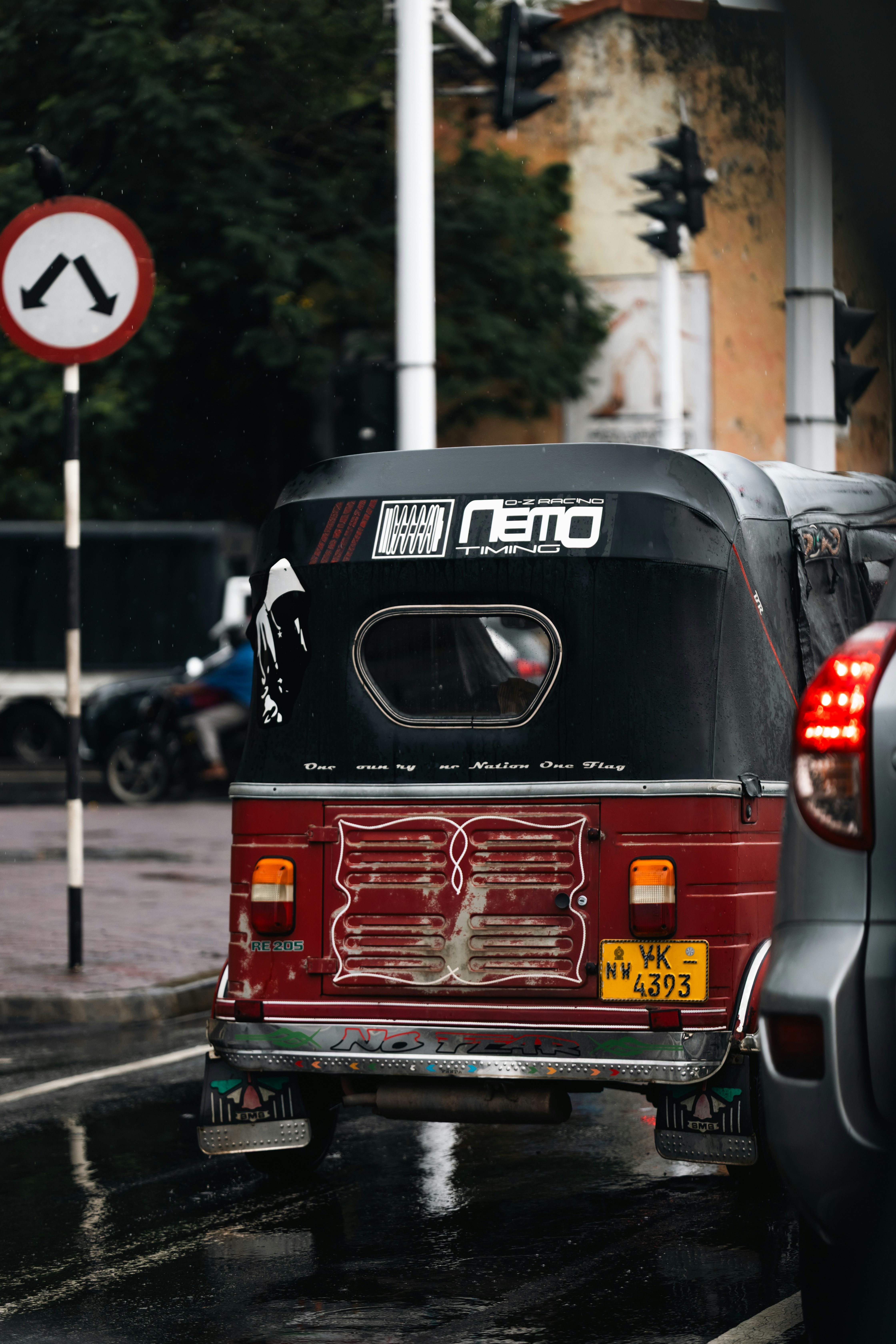 Red and black tuk-tuk driving on wet street