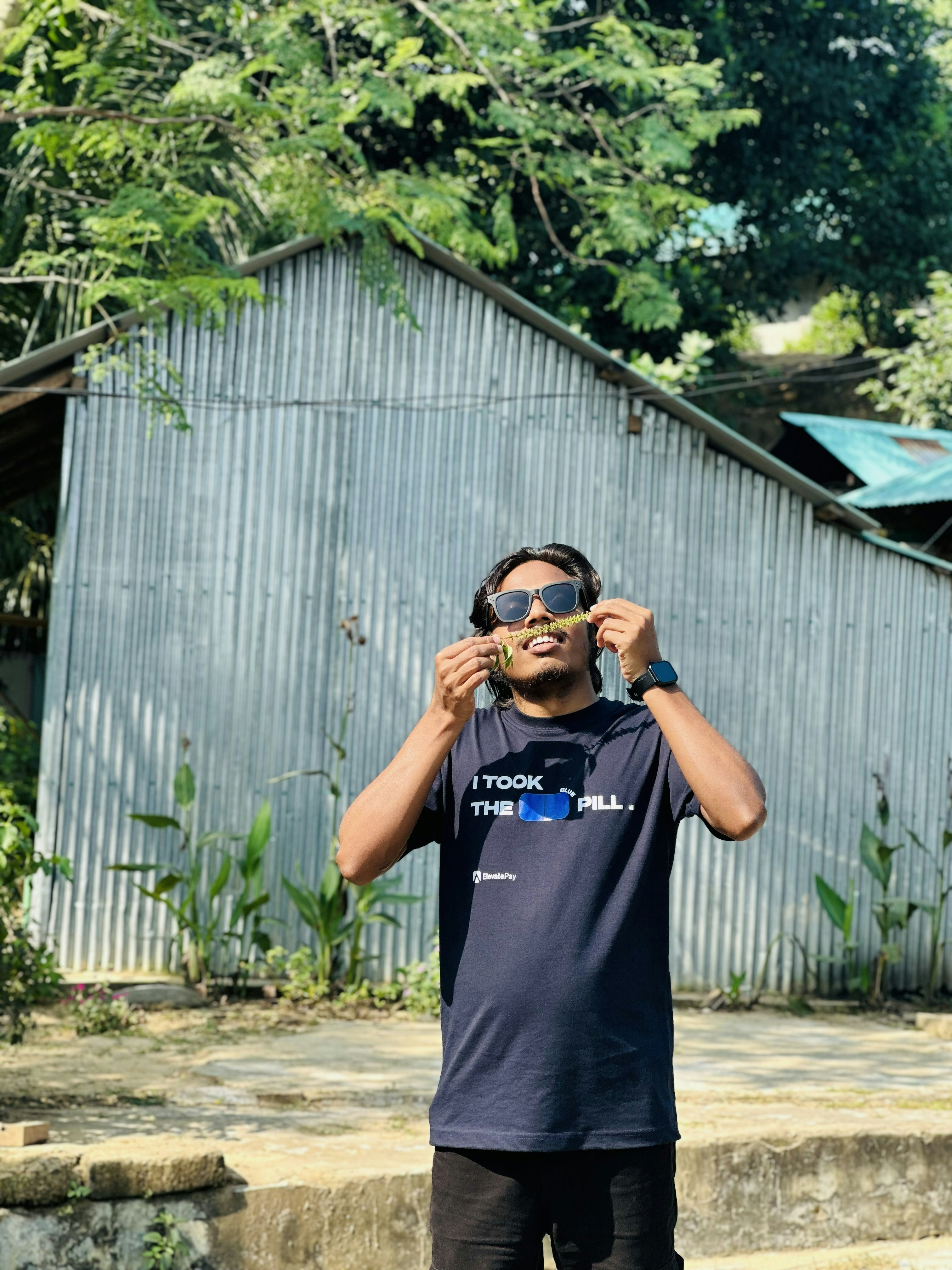 Pria memegang ranting di depan bangunan logam bergelombang.