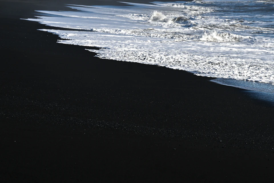 Serene beach scene with black sand shoreline contrasting with light blue ocean waters