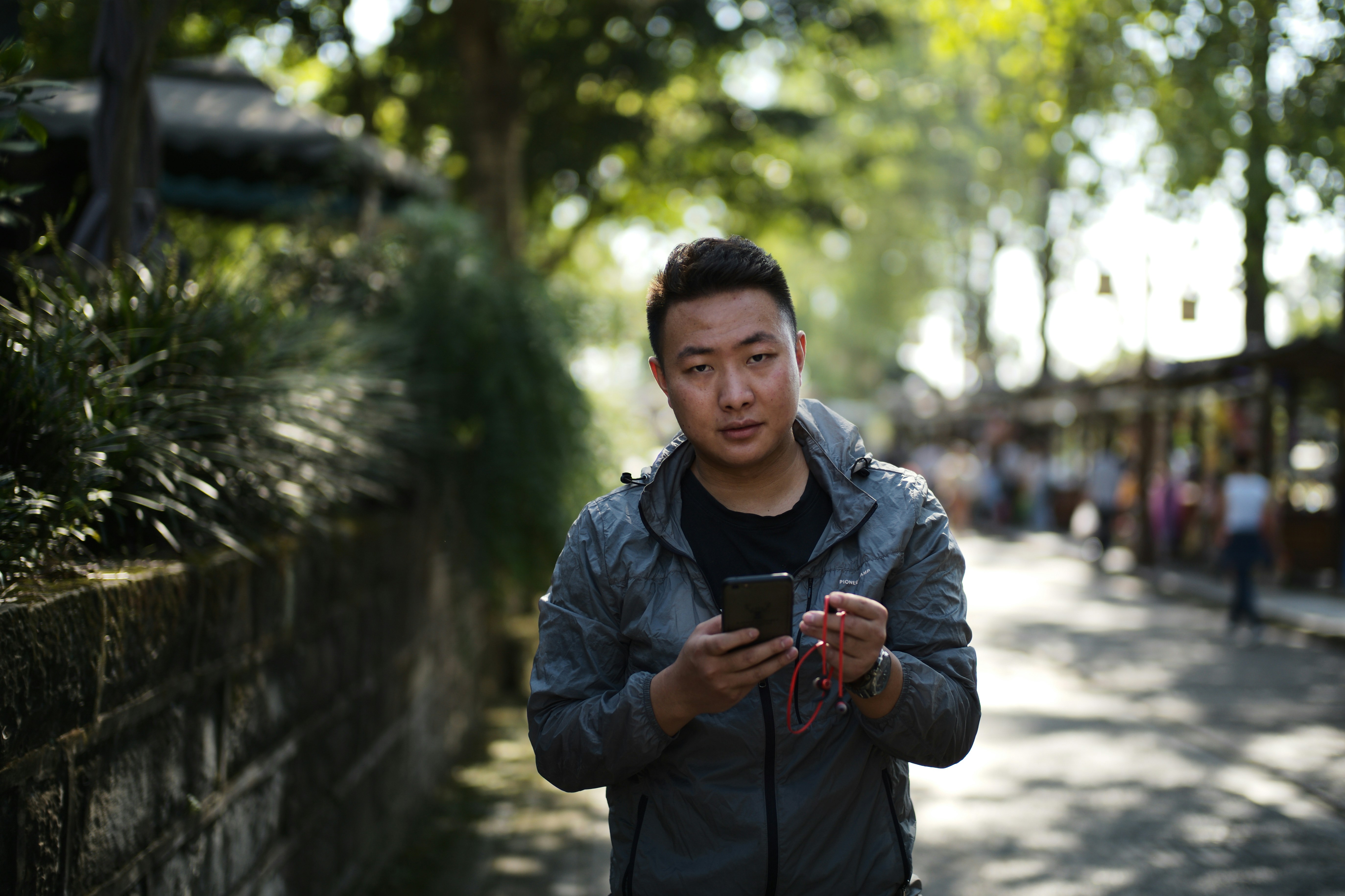 A man holding a smartphone outdoors on a sunny day.