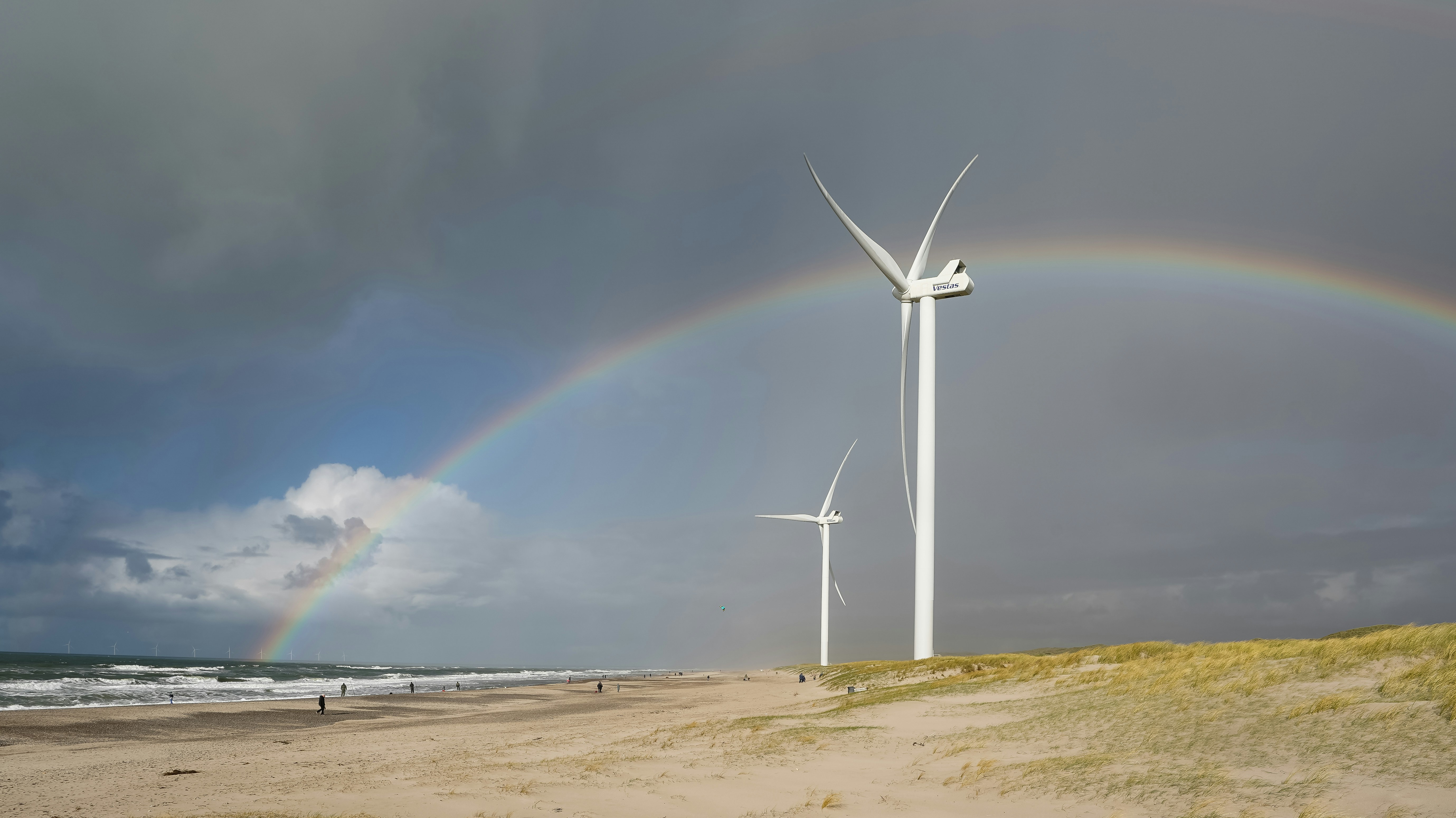 Wind turbines on a beach with a rainbow.