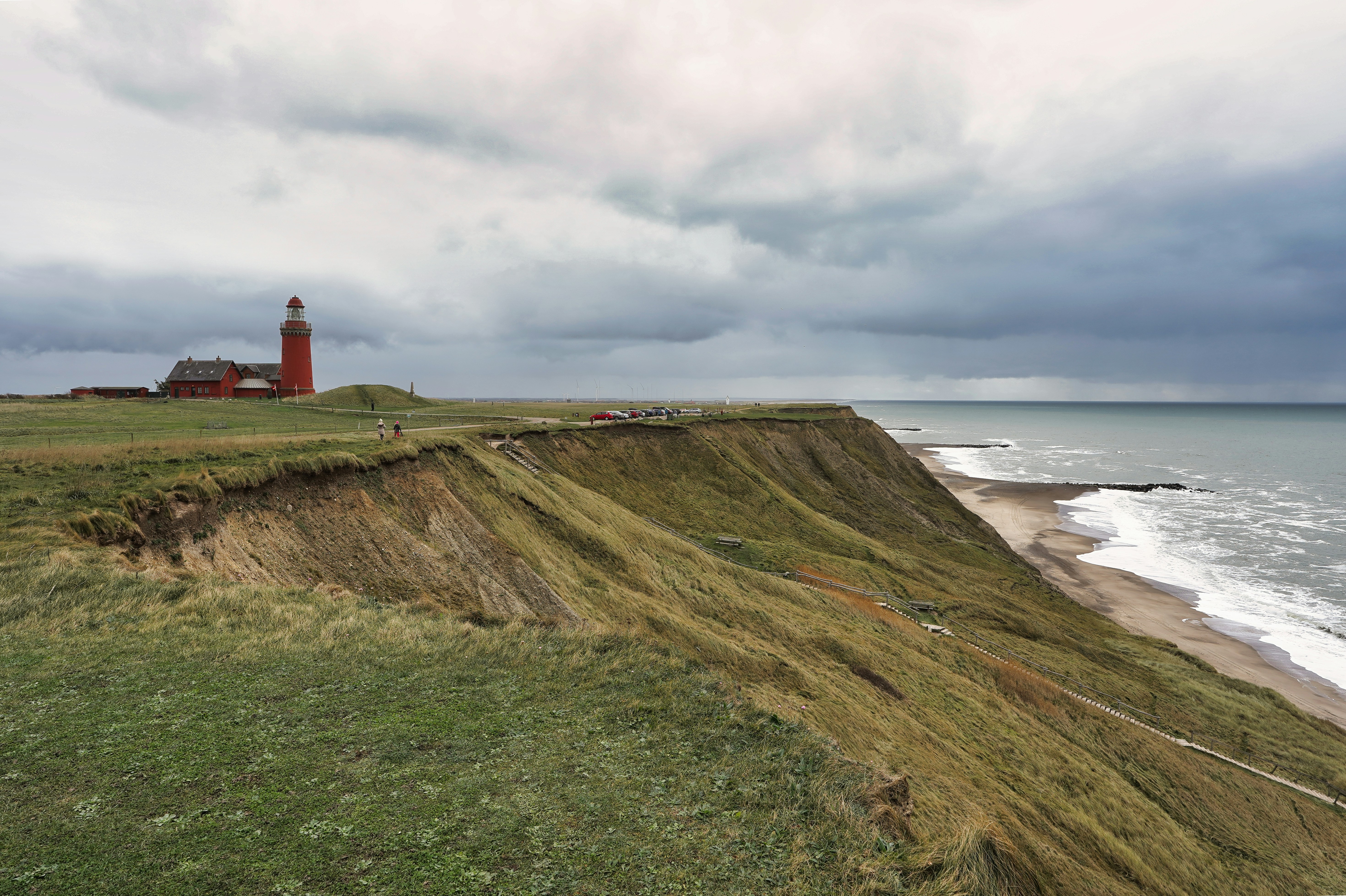 Red lighthouse on grassy cliff overlooking the sea
