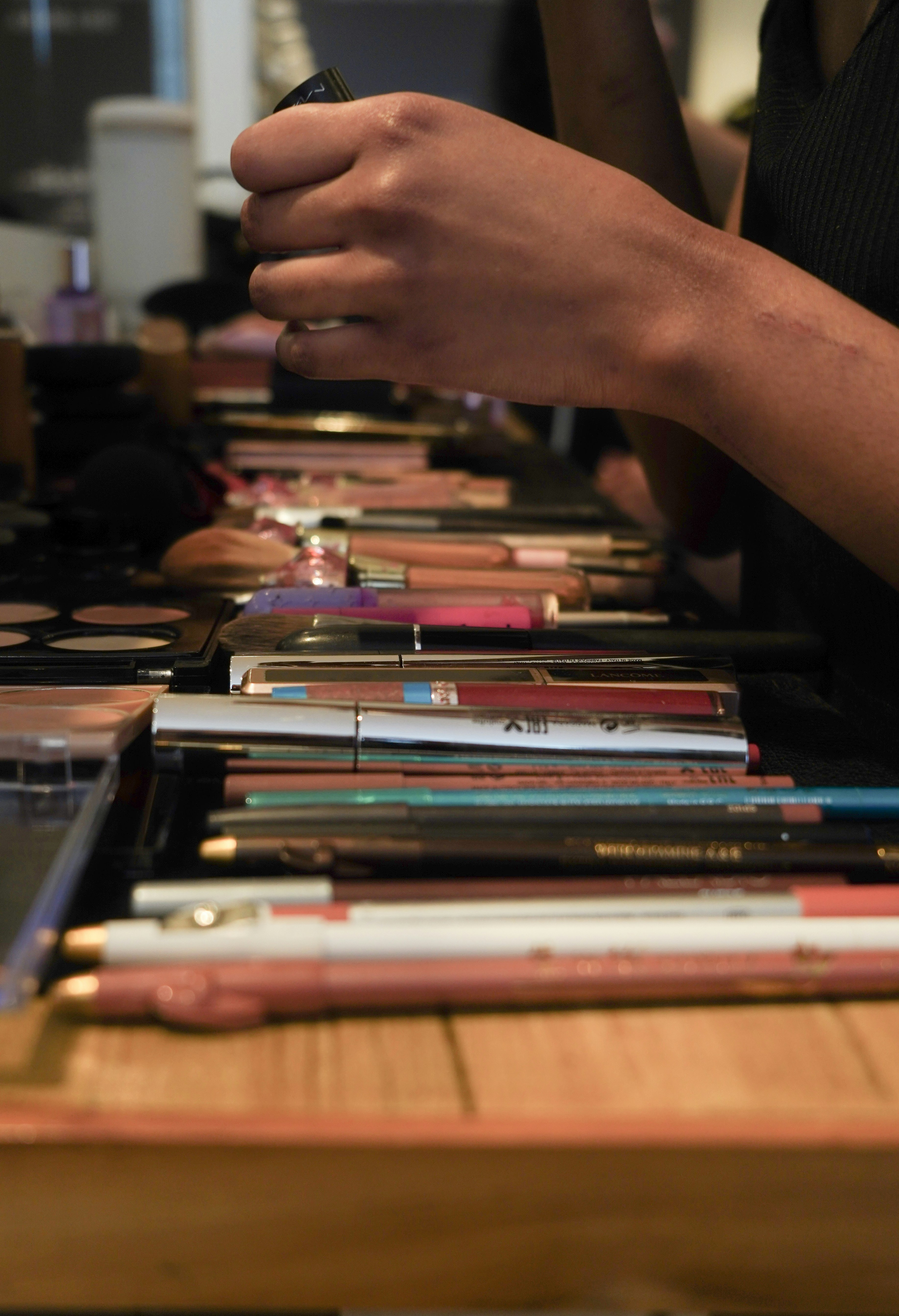 Hands arranging makeup brushes and cosmetics on a table