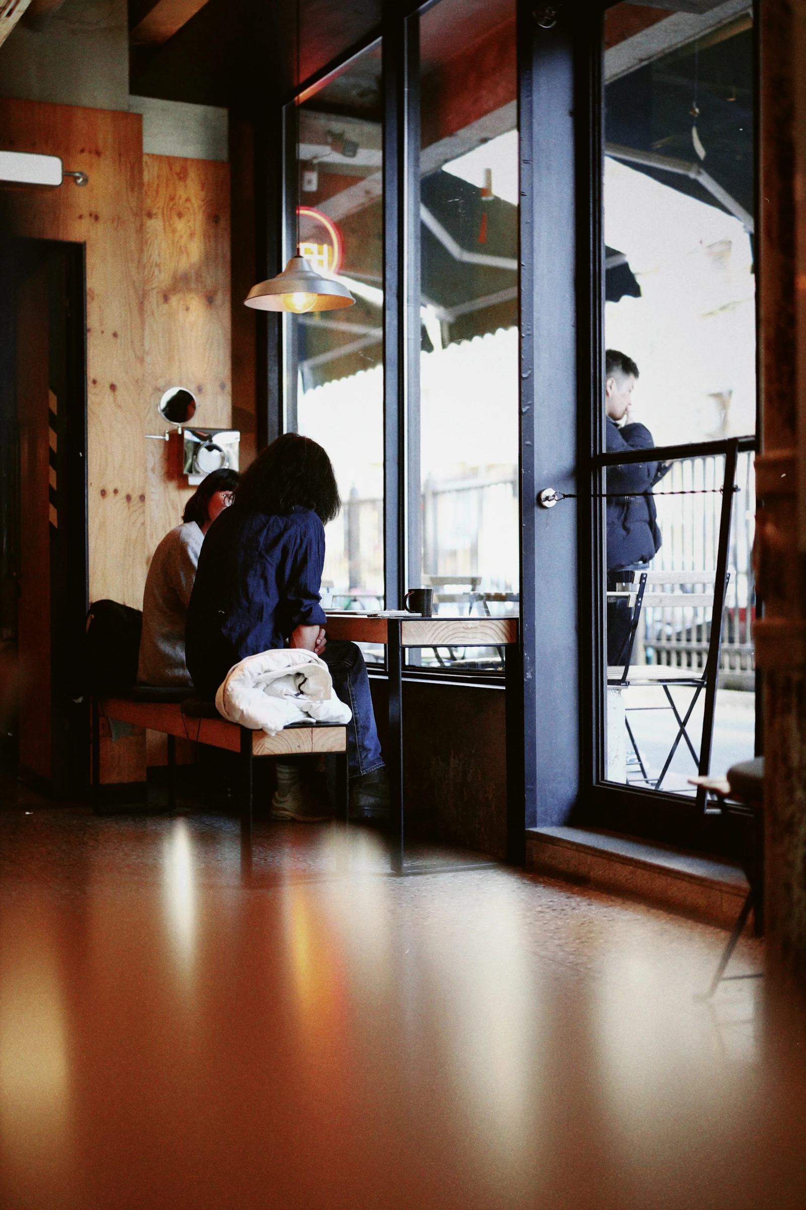 Two people sit at a small café table beside a tall window.