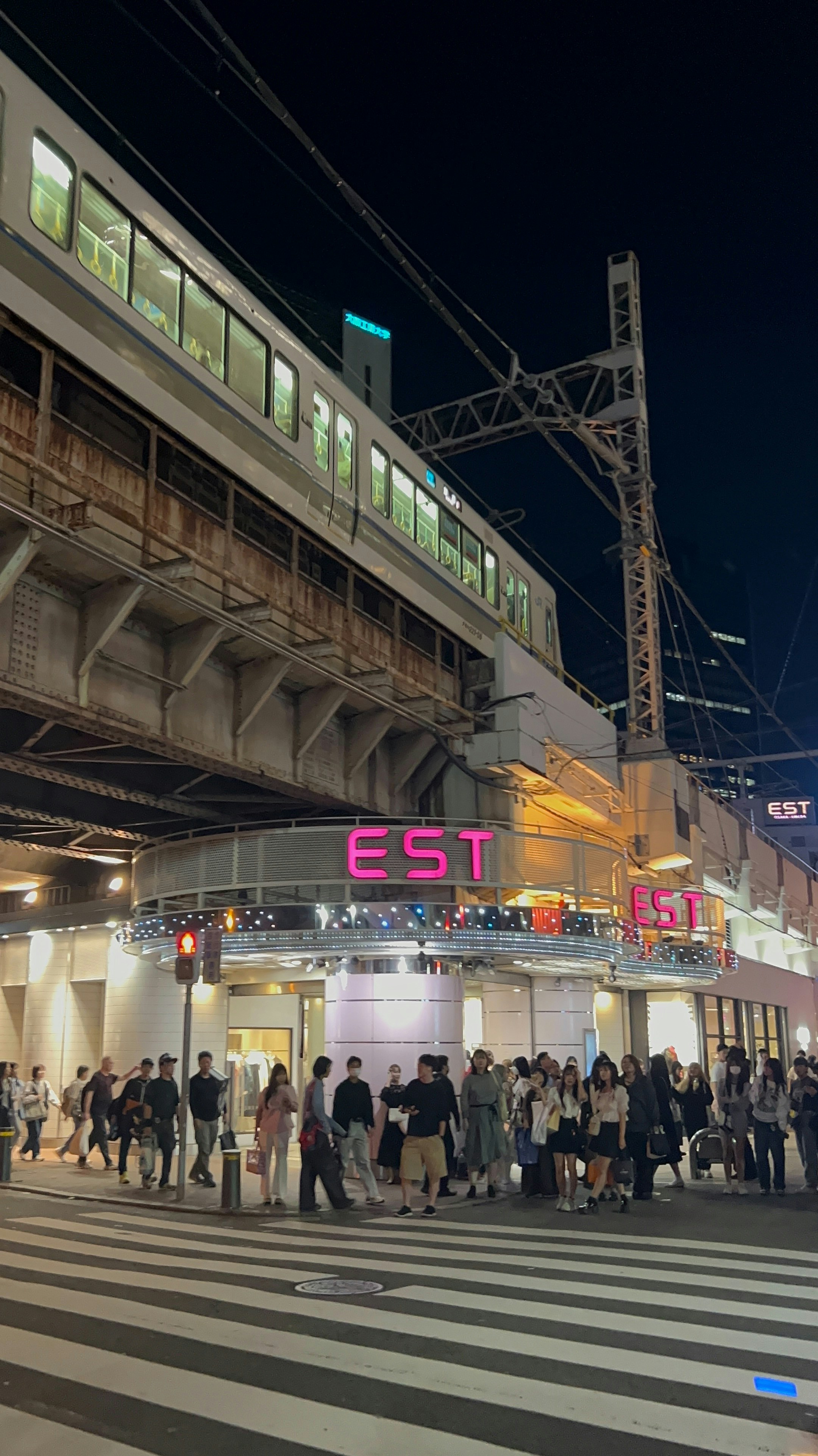 People crossing street at night near est building and train.
