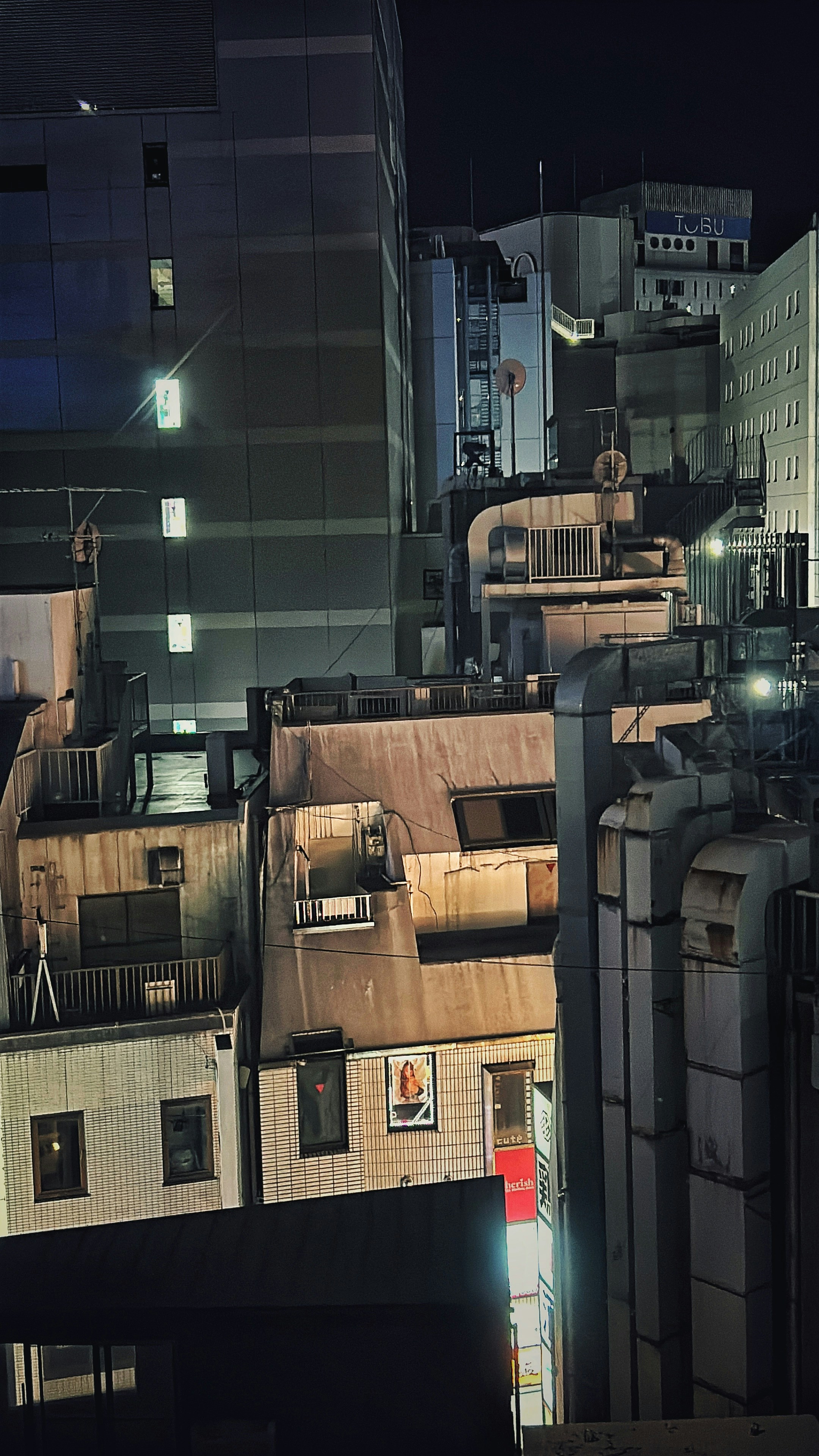 Buildings at night with illuminated windows and pipes.