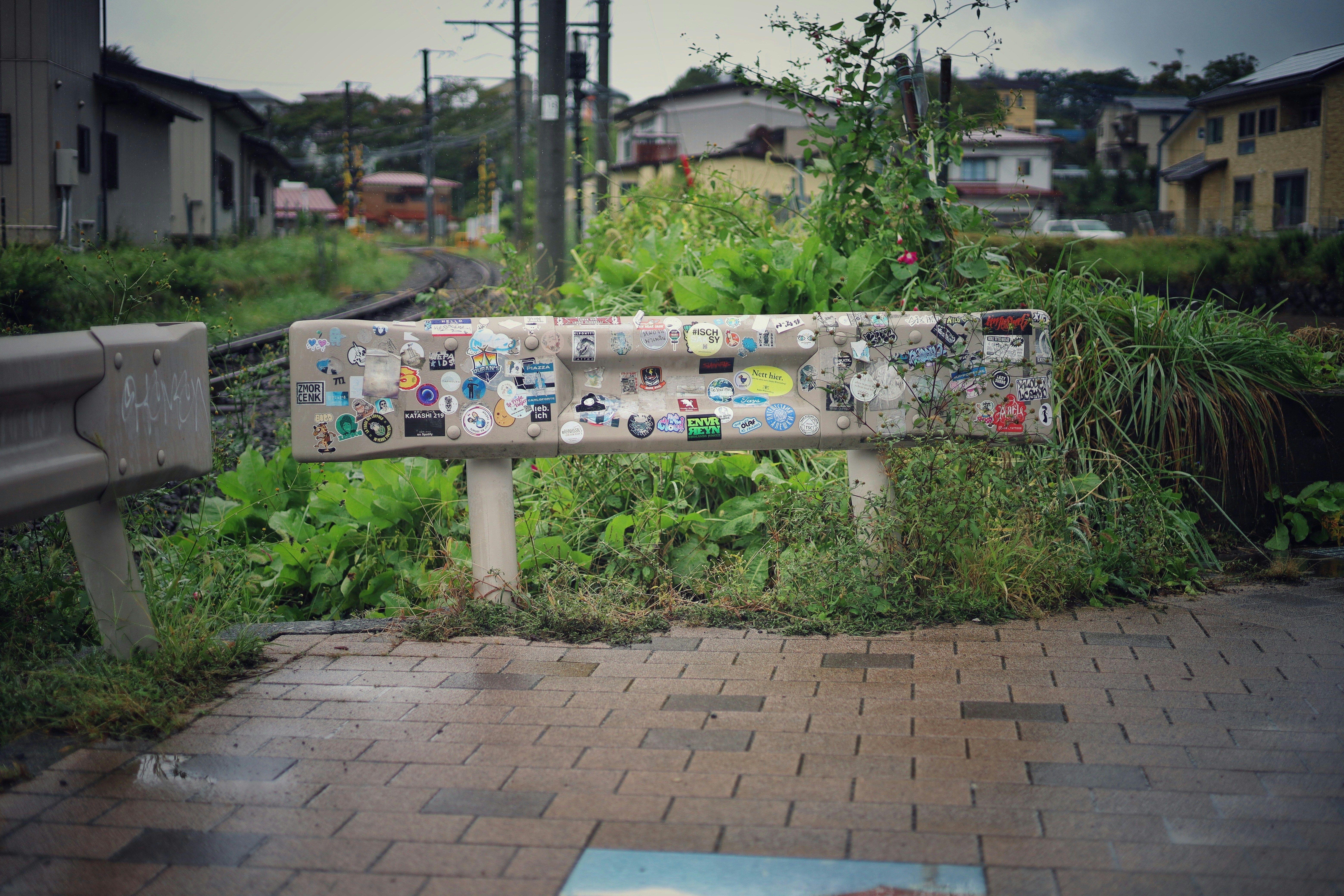 Concrete barrier covered in stickers with overgrown plants.