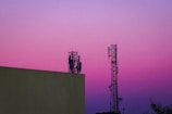Two cell towers against a purple and pink sky.