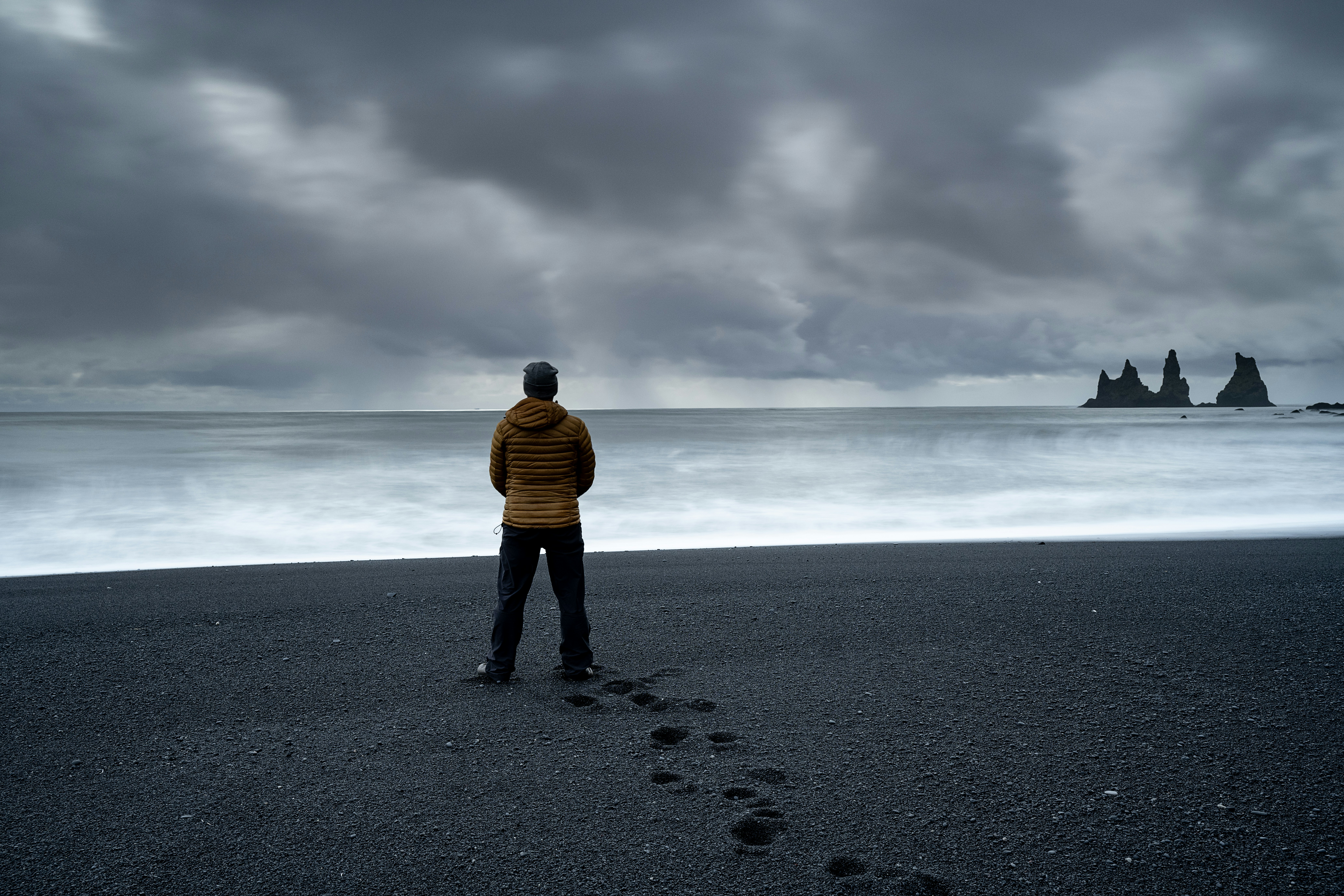 Person standing on black sand beach looking at ocean