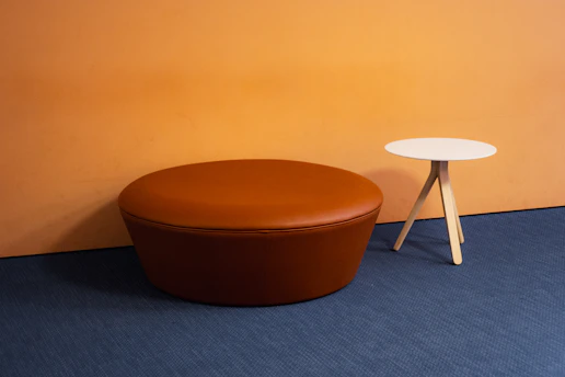 Brown ottoman and small side table against orange wall