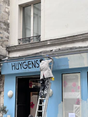 Person painting a blue storefront on a ladder