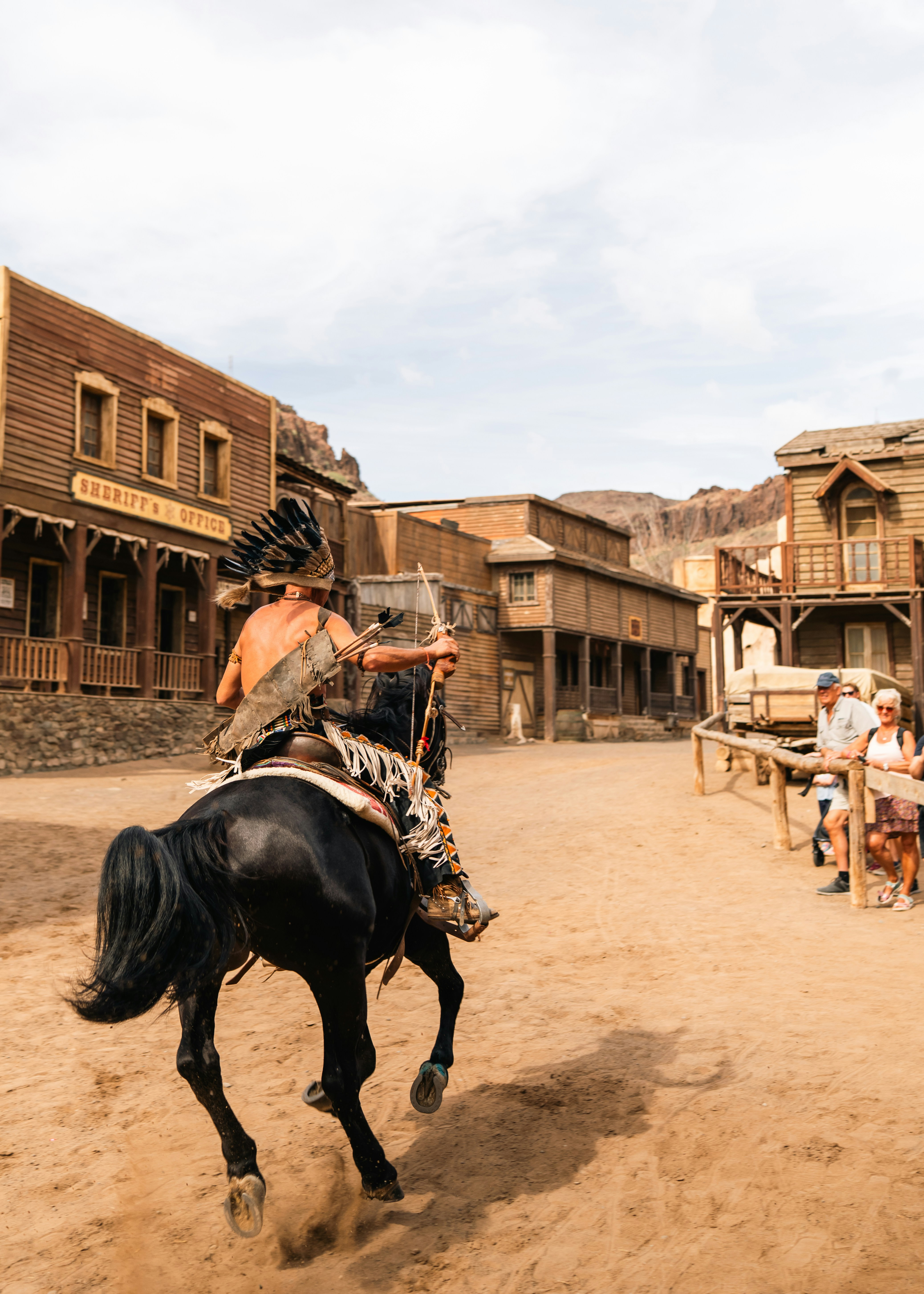 Man in native american attire on horseback in western town.