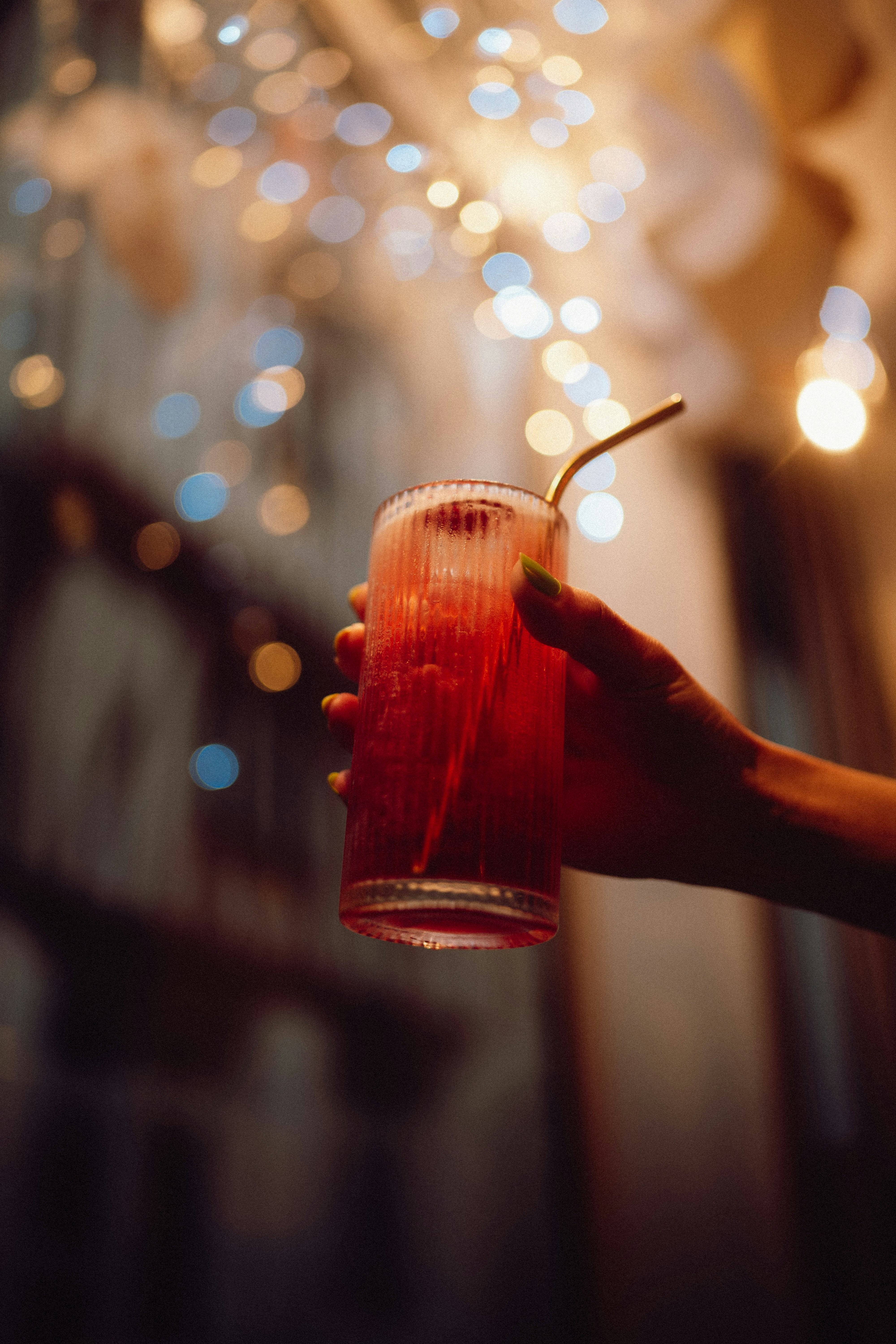 Hand holding a red cocktail with bokeh lights