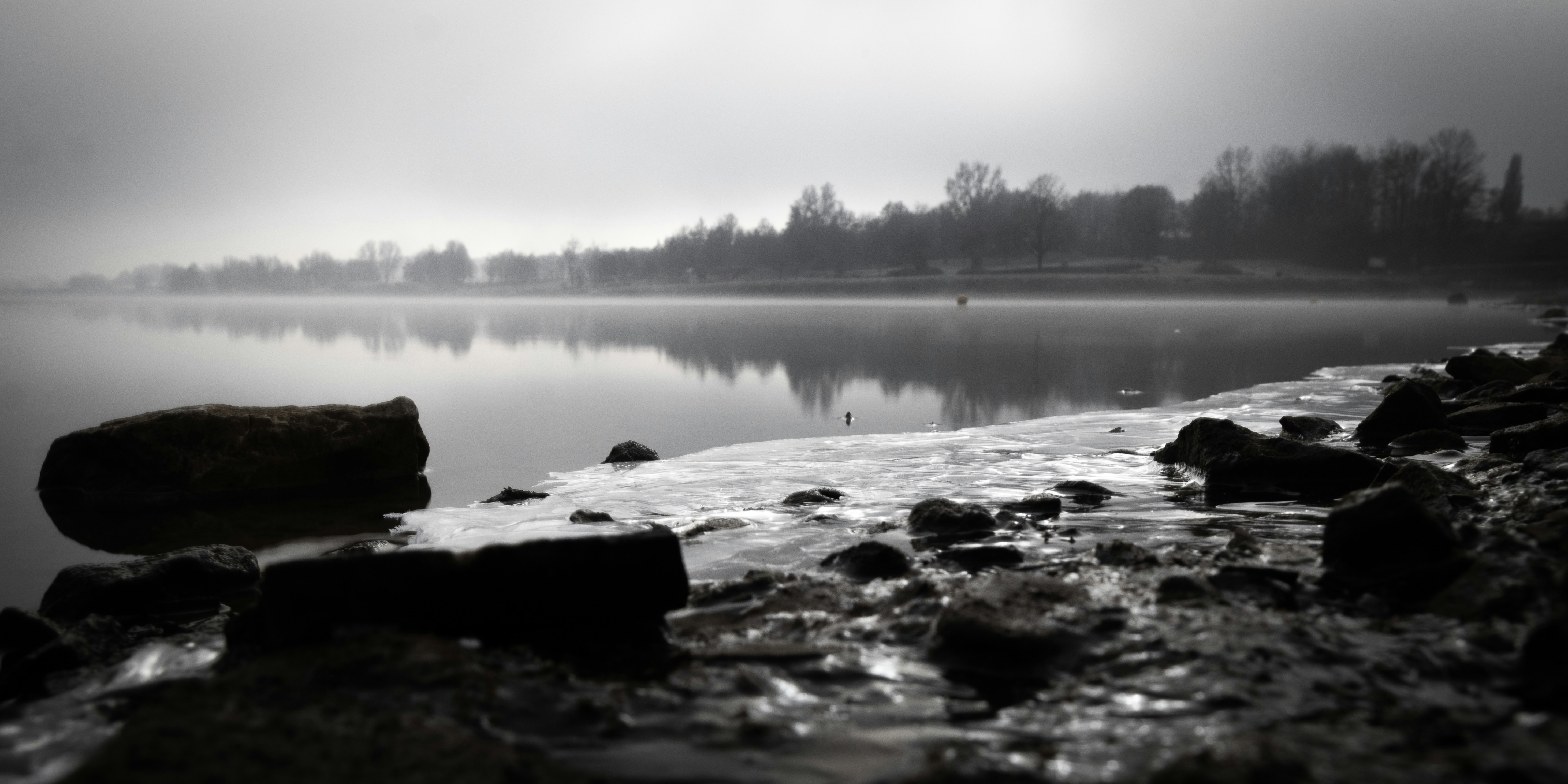 Misty lake with rocky shore and distant trees