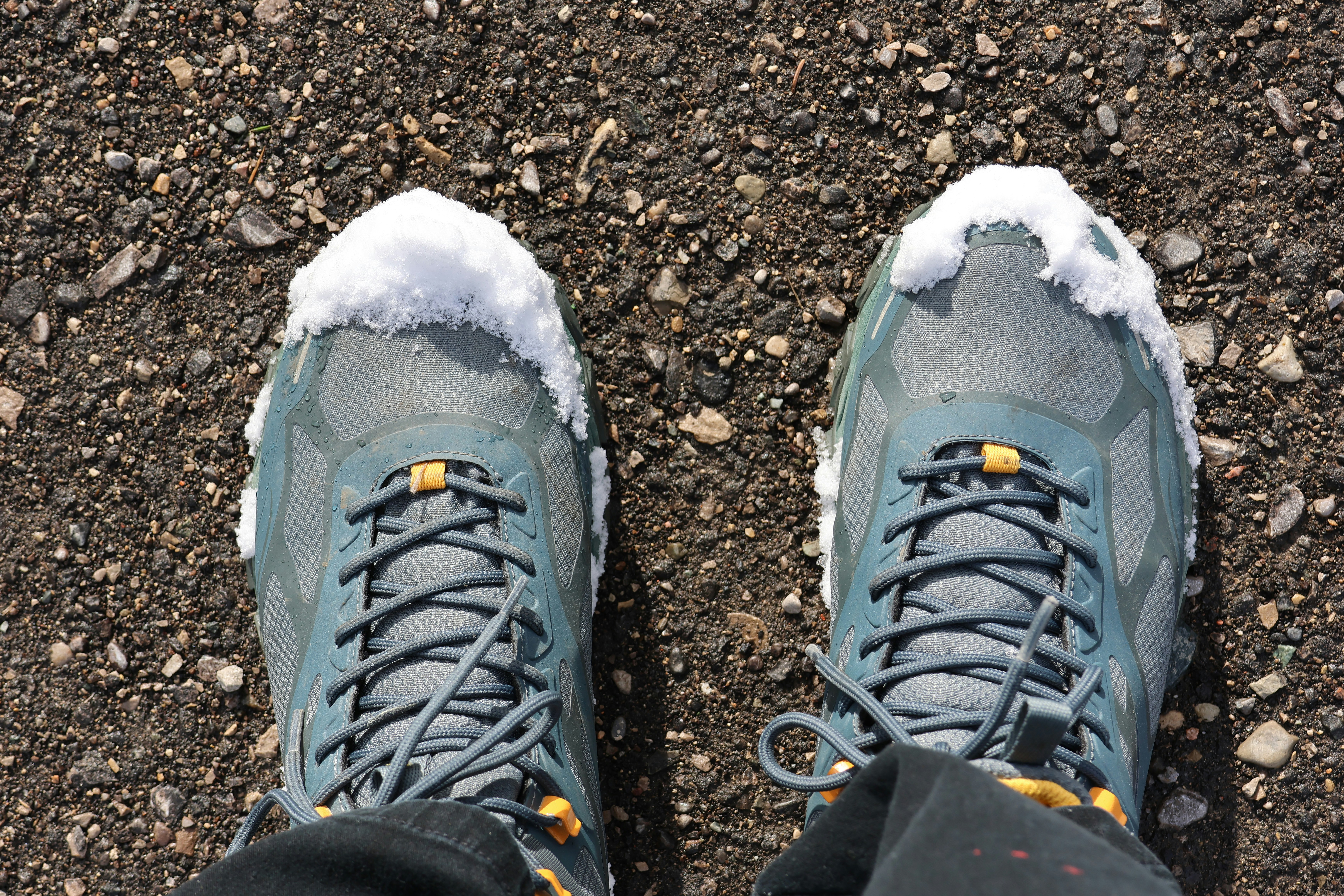 Hiking Boots Covered in Fresh Snow on Gravel Trail in Winter Sunlight