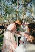 Woman in floral dress signing document at outdoor wedding.