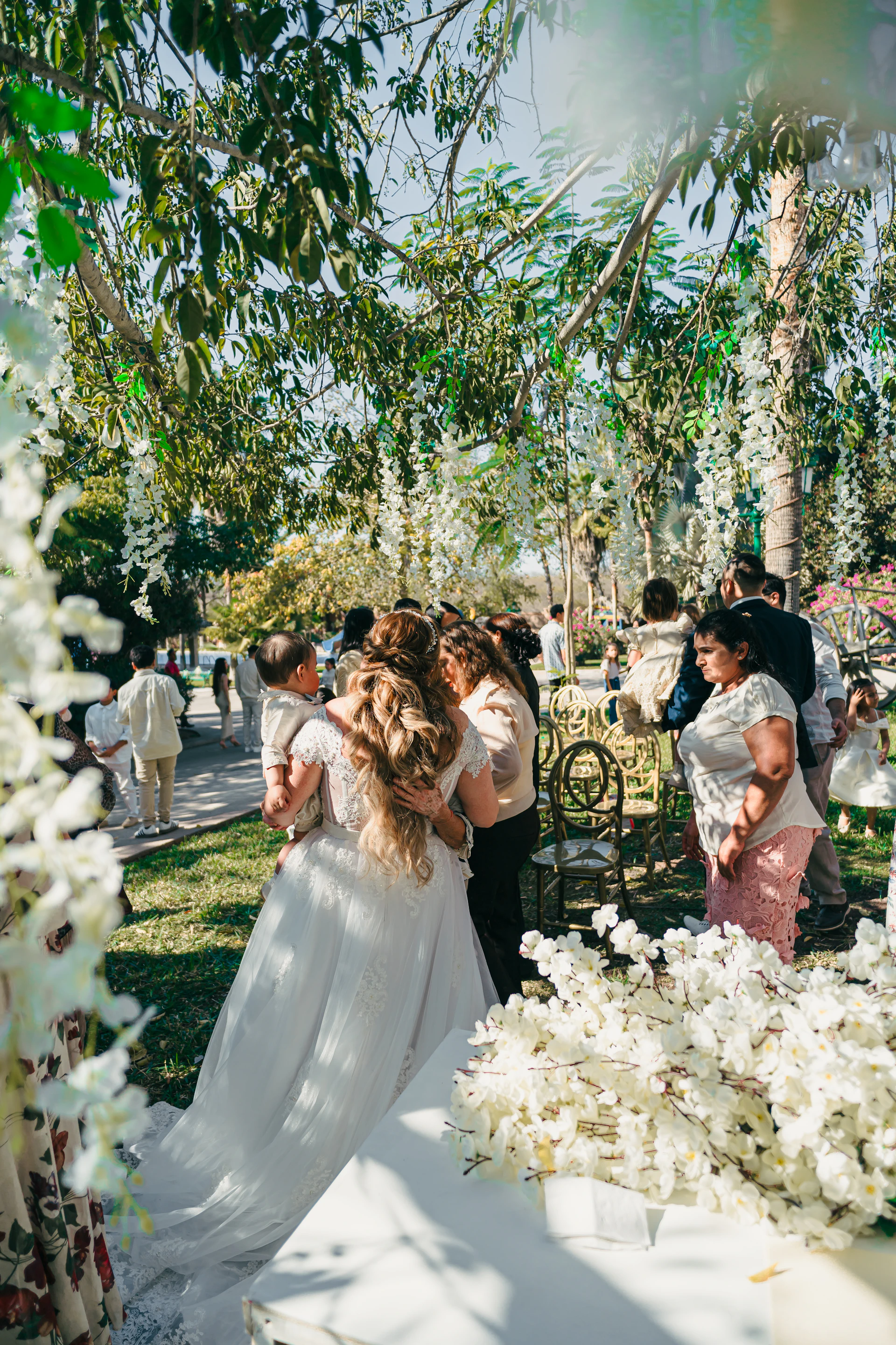 Wedding guests gather outdoors under floral decorations