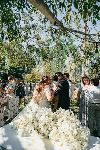 Bride and groom hug child at outdoor wedding ceremony.