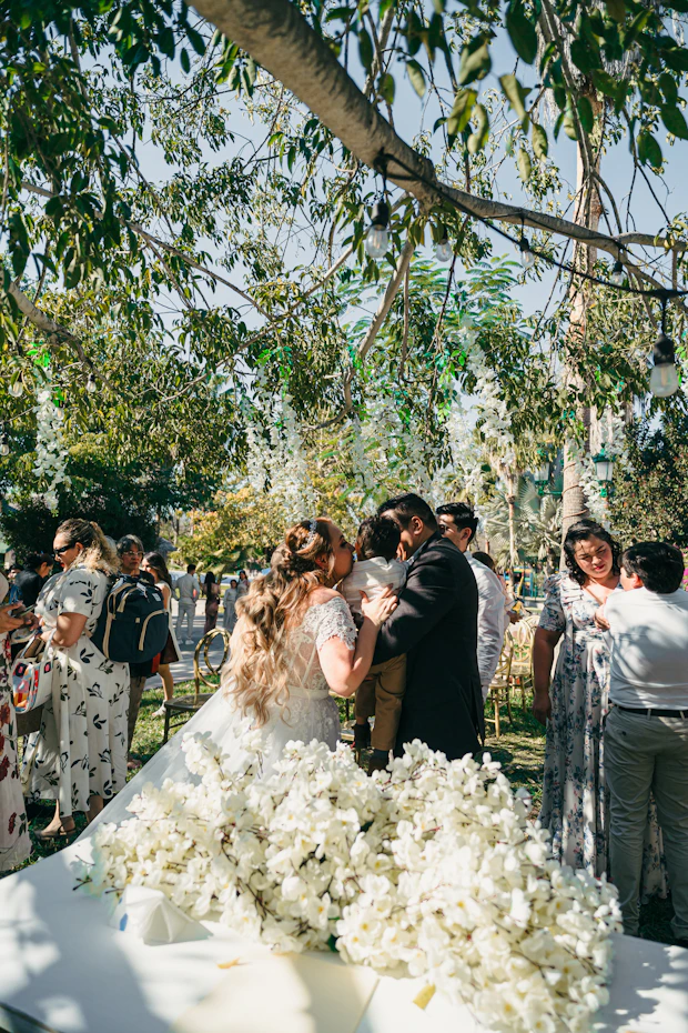Bride and groom hug child at outdoor wedding ceremony.