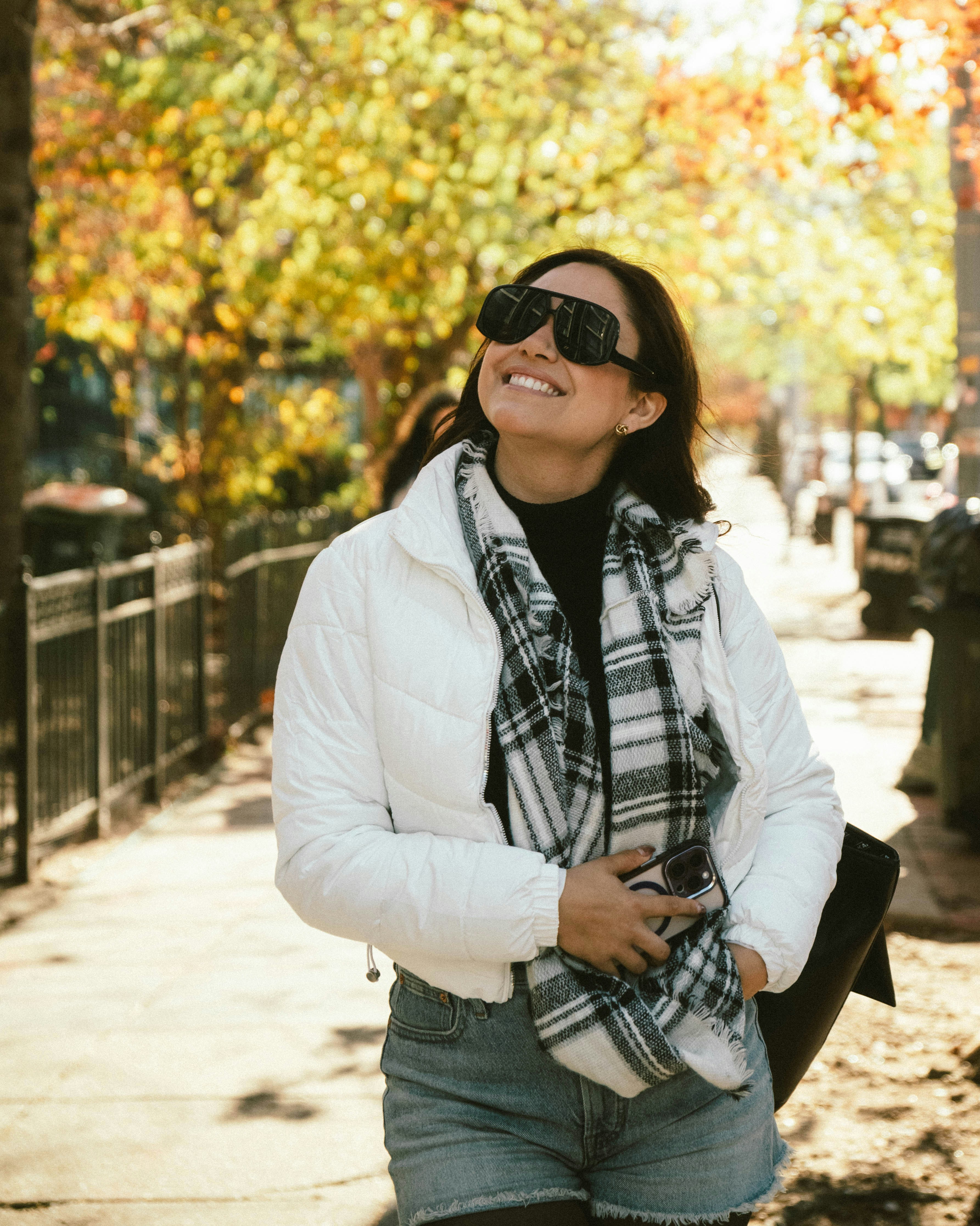 Mujer caminando por una acera rodeada de árboles otoñales.
