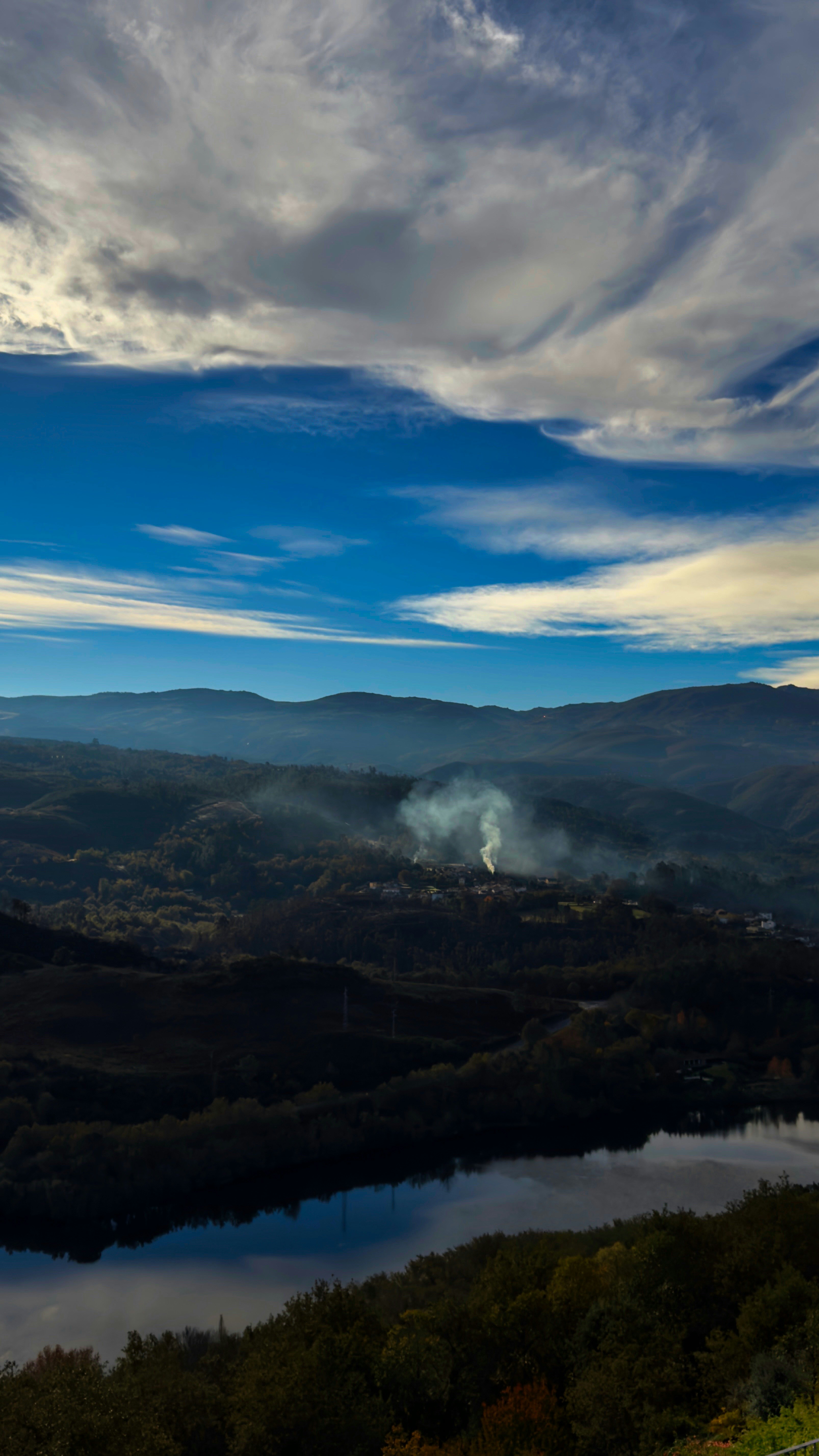 Smoke rises from a village nestled in rolling hills.