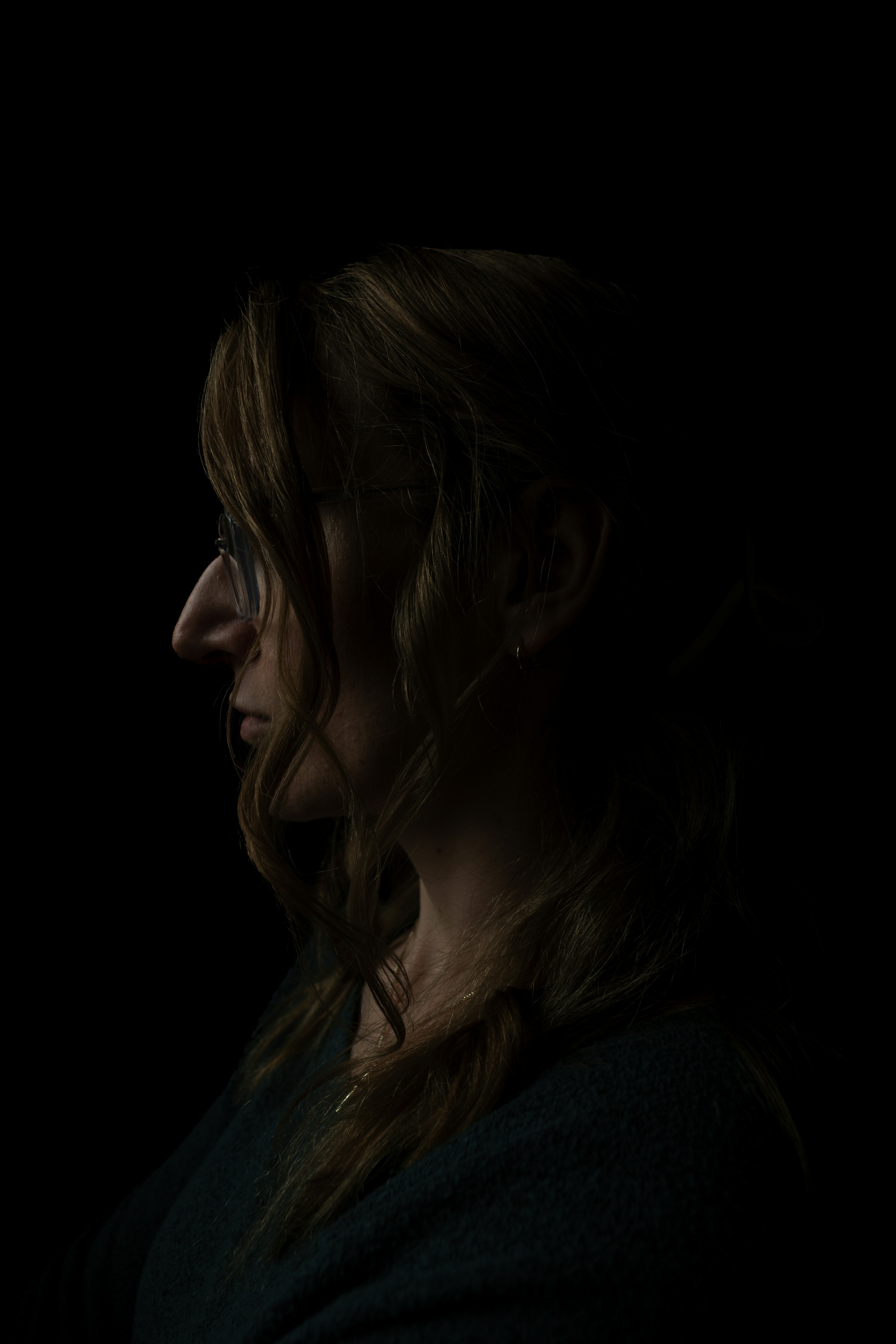 Profile of a woman with glasses in calm, low light, suggesting reflection and emotional self-awareness.