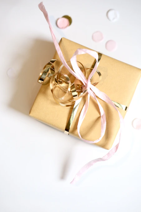 A golden gift box tied with pink and gold ribbons