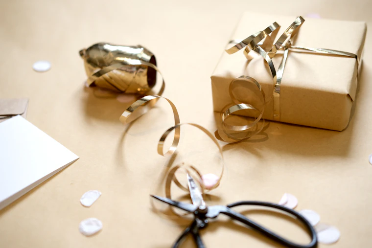 Regalo envuelto en papel kraft con lazos dorados, tijeras y confeti