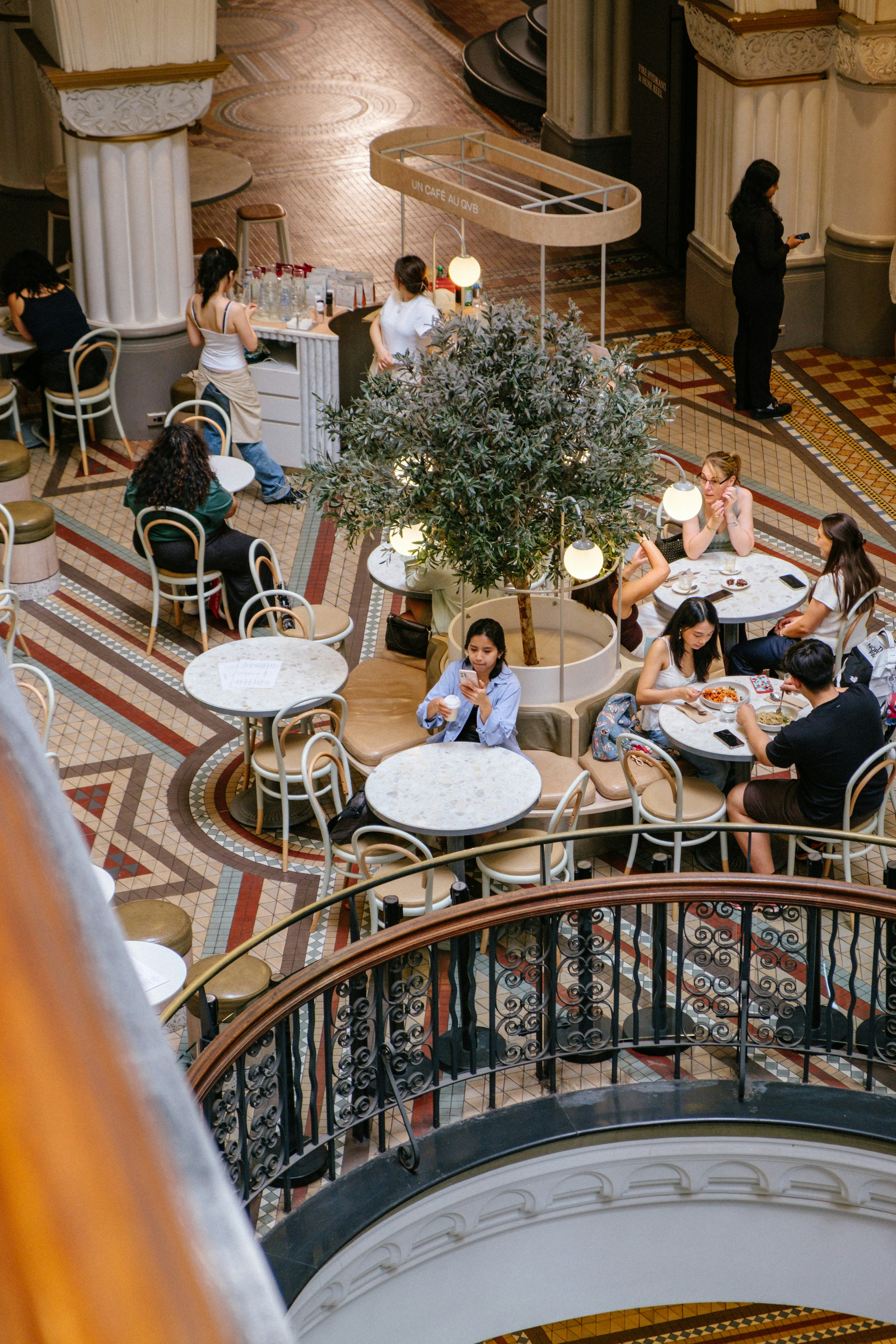 Gente cenando en mesas en un espacio interior luminoso y ornamentado.