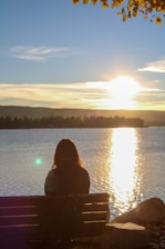 Woman sitting on bench overlooking lake at sunset.
