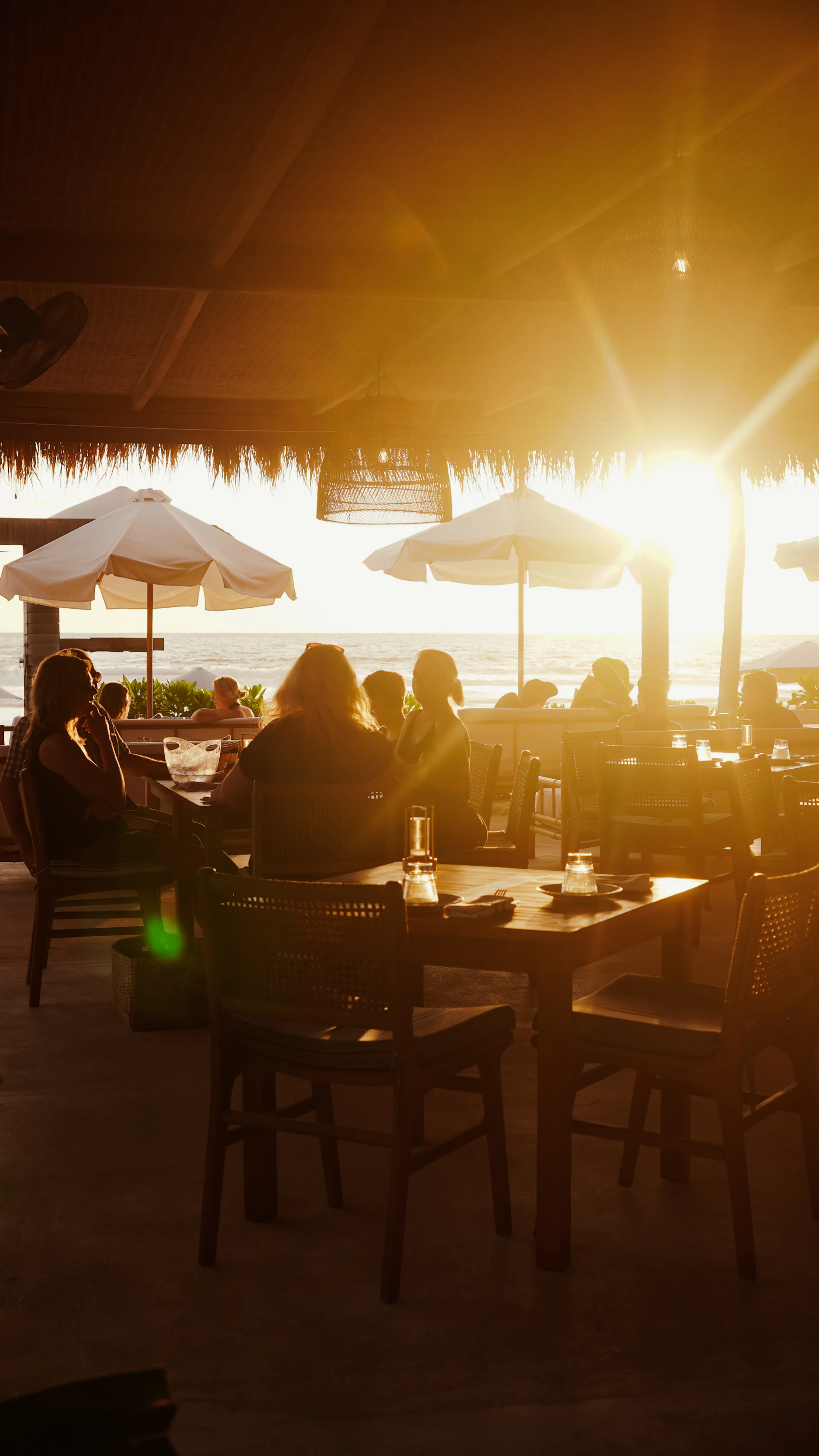 Guests dining at a relaxed beachside restaurant at sunset