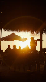 Silhouette of people at tables under umbrellas at sunset.