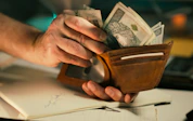 Hands holding us dollar bills in a brown leather wallet