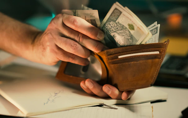 Hands holding us dollar bills in a brown leather wallet