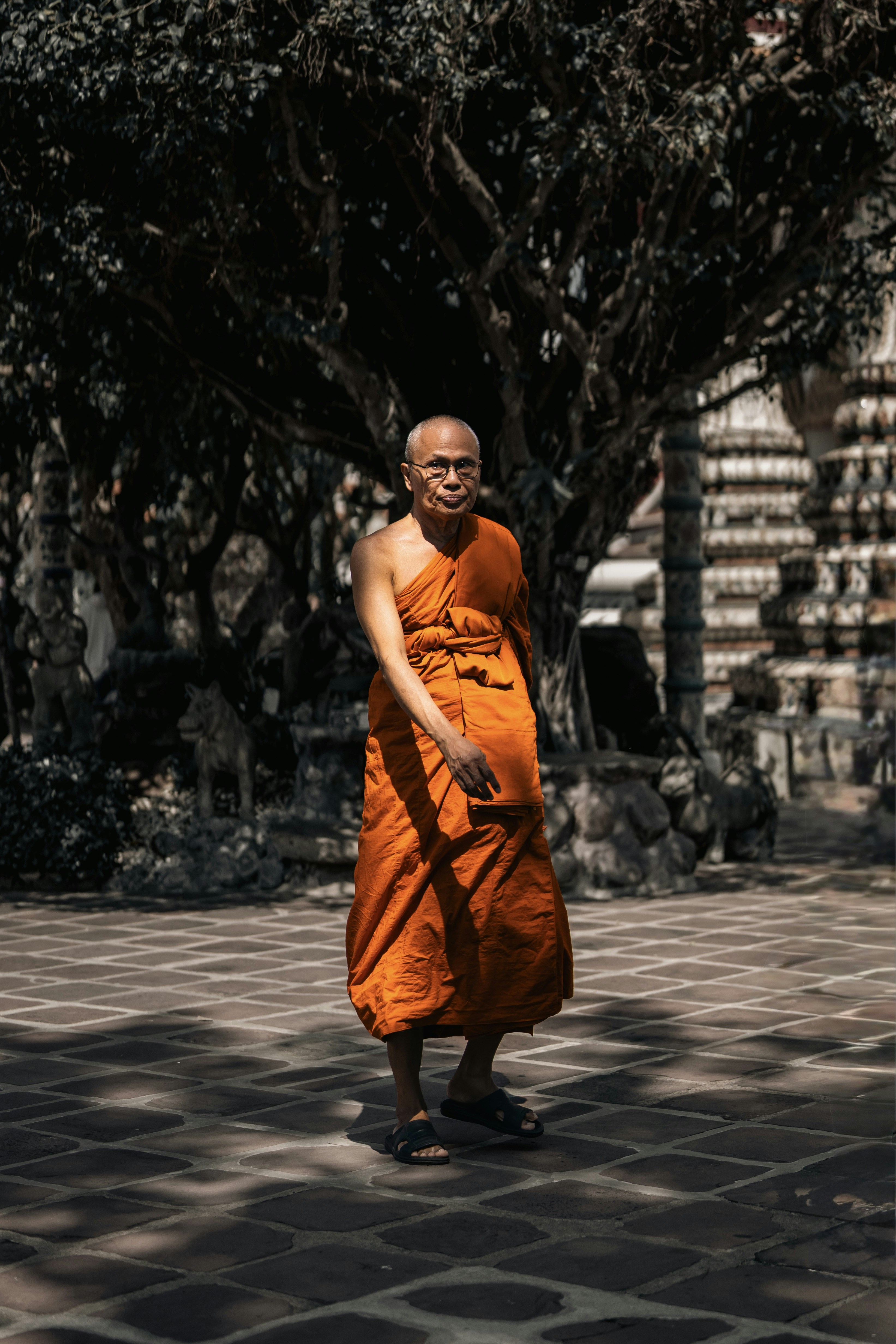 A buddhist monk in orange robes walks outdoors.
